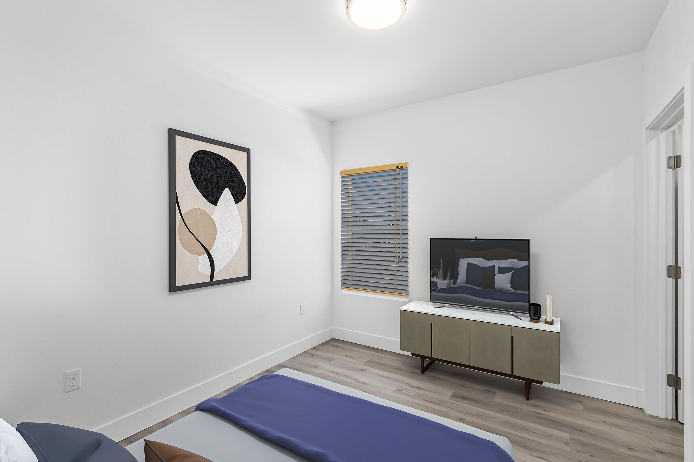 A modern bedroom featuring a neatly made bed with a blue throw blanket, a flat-screen TV on a minimalist console, and a large piece of abstract art on the wall. There's a window with blinds allowing natural light and a ceiling light fixture illuminating the space. The walls are painted white, creating a bright atmosphere.