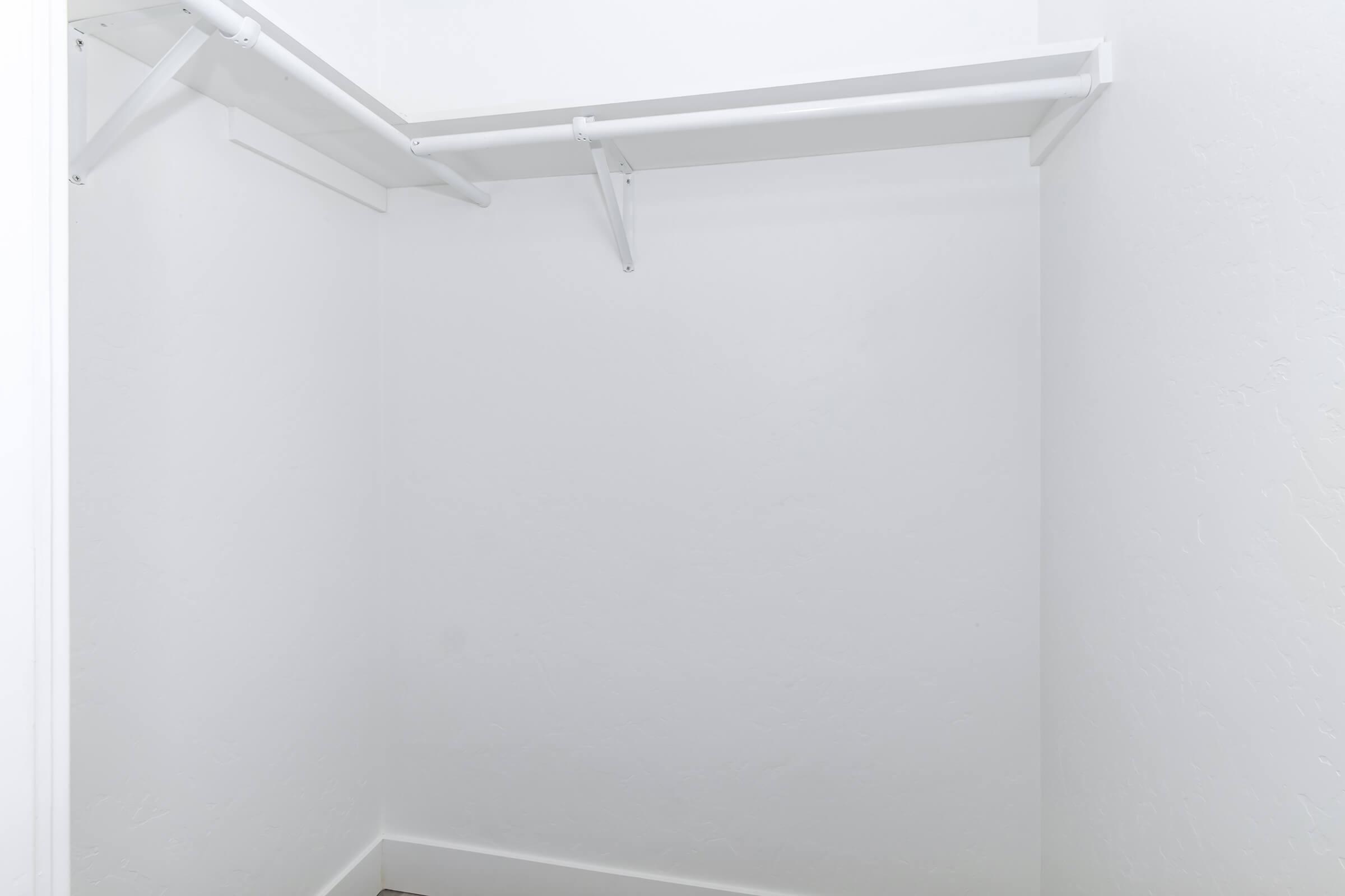 Empty closet with white walls and a double hanging rod. The space has no shelves or other storage features, creating a minimalist and clean appearance. The floor is unobstructed, and the overall design emphasizes simplicity and openness.