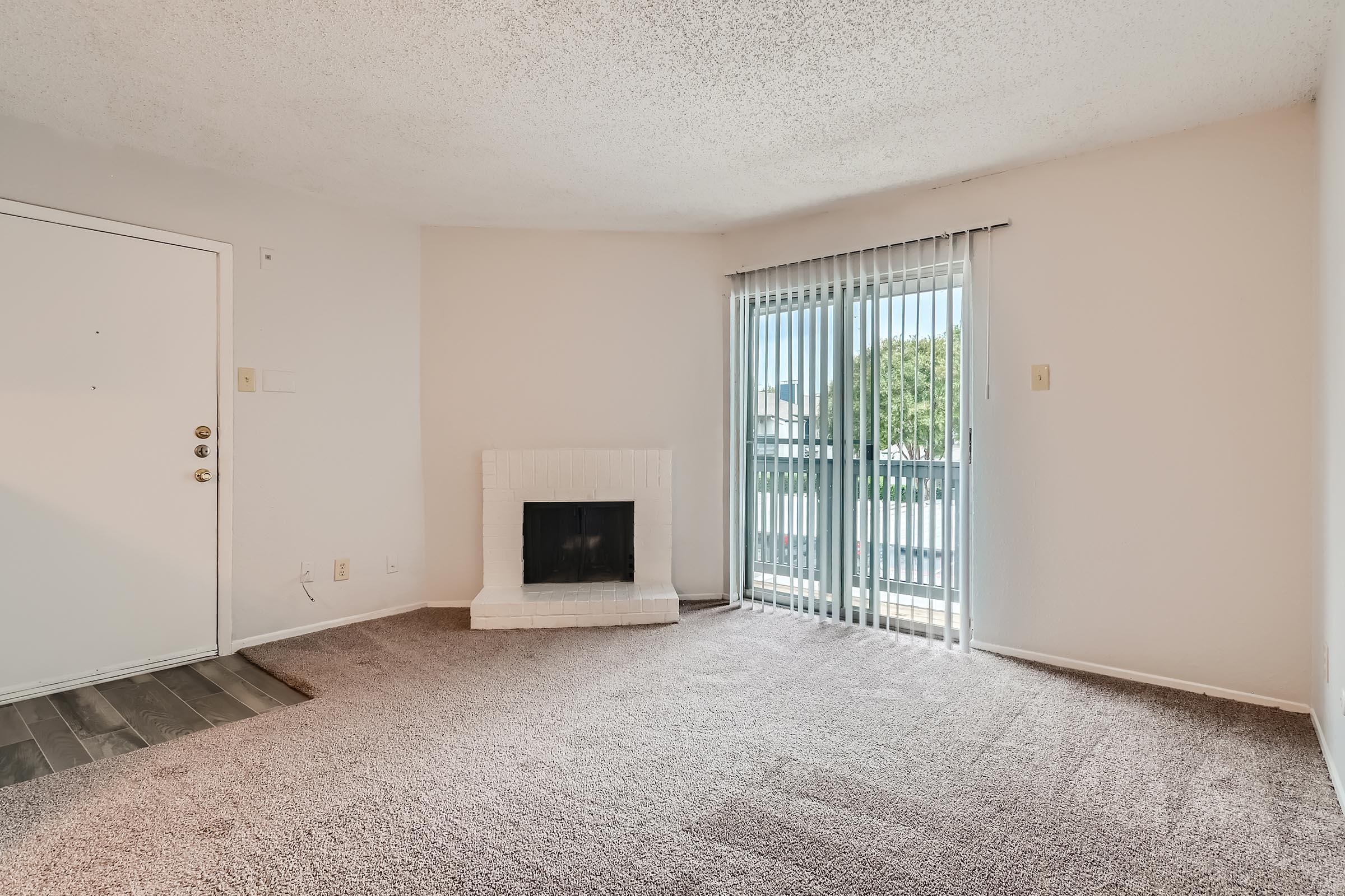 A carpeted living room with a fireplace and a balcony at Rise North Arlington in Arlington, TX.