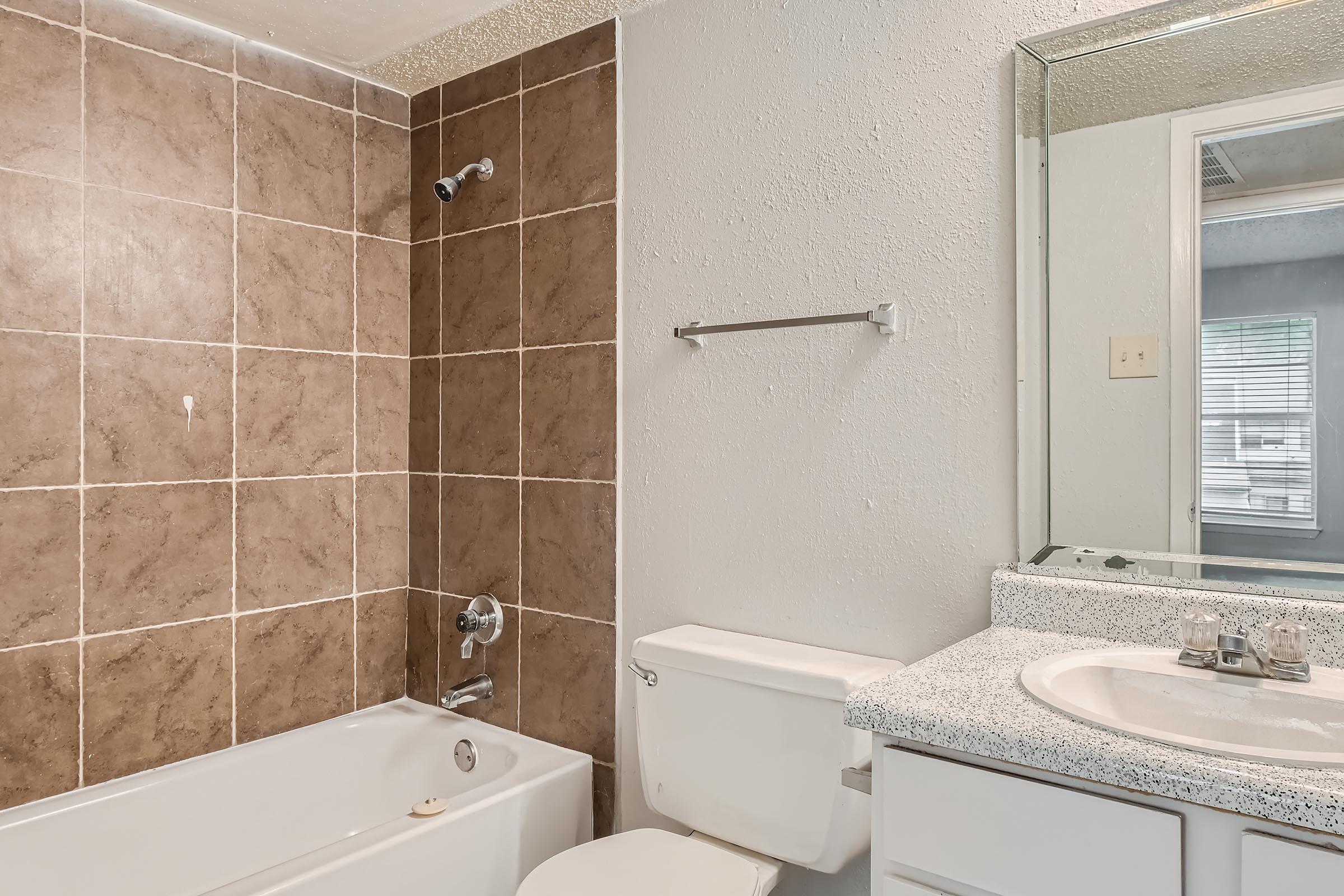 An apartment bathroom with brown tiling in the tub area at Rise North Arlington.