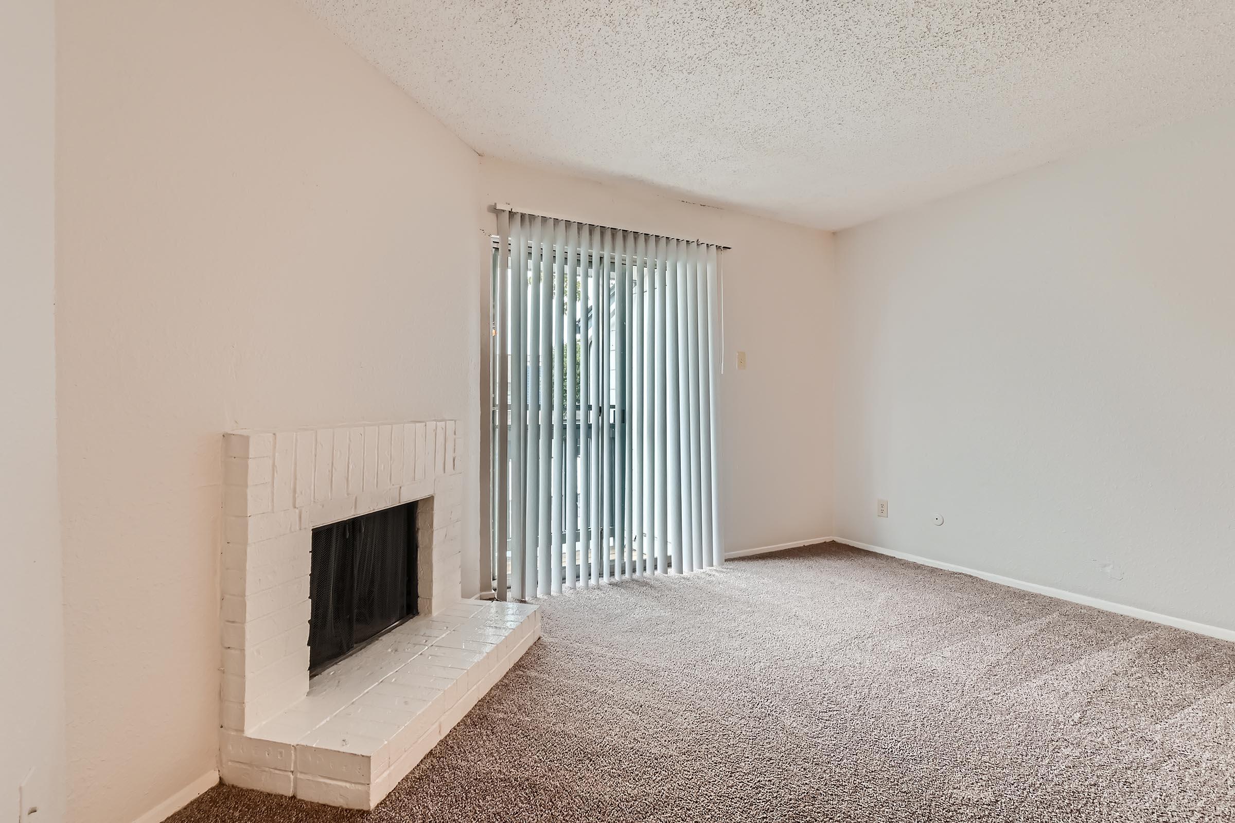 An apartment living room with carpeting, a fireplace and glass doors leading to a balcony at Rise North Arlington.