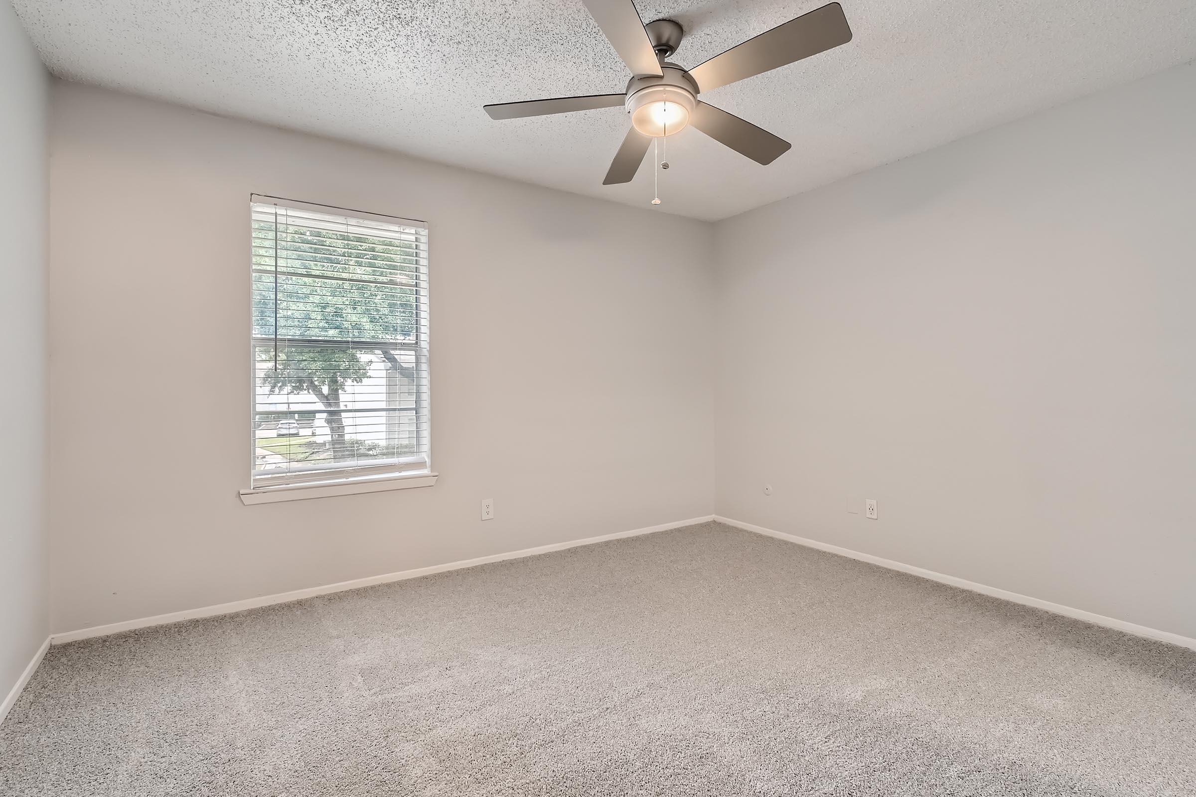 A carpeted bedroom with a ceiling fan and a window at Rise North Arlington.