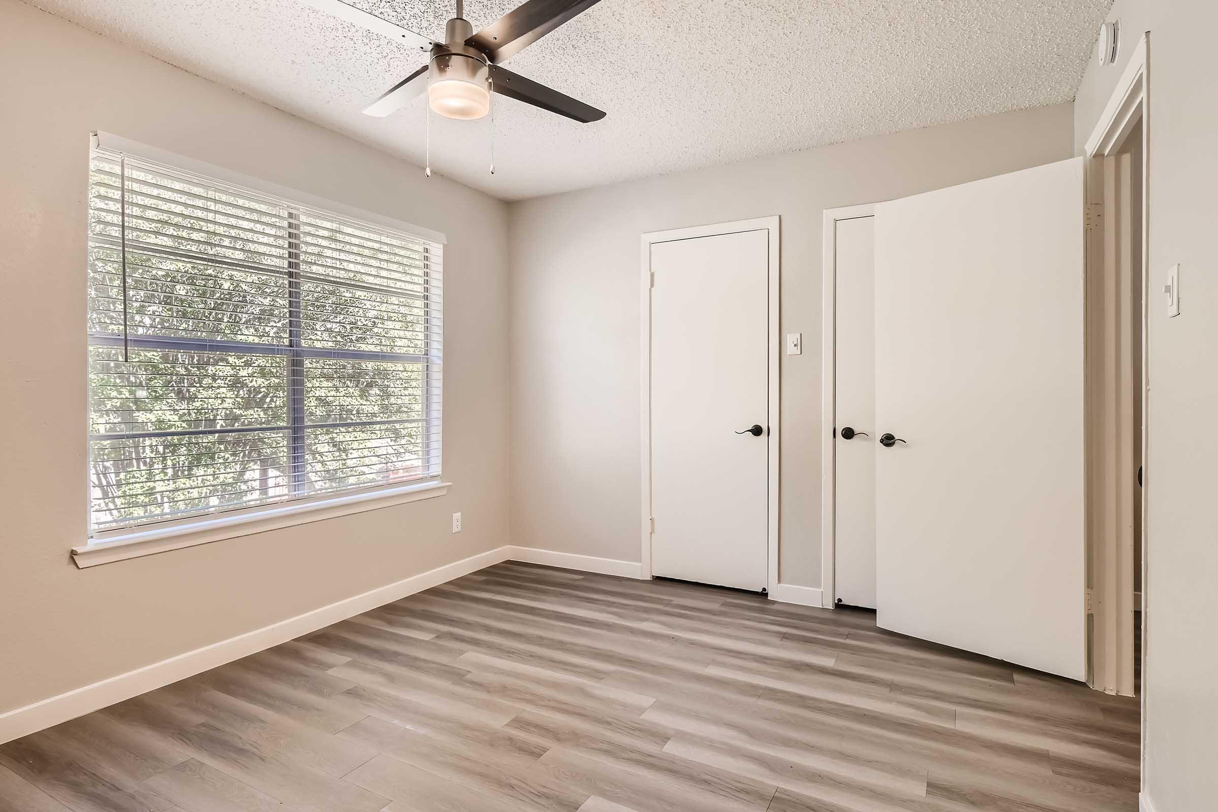 An apartment bedroom with wood-style flooring, a ceiling fan, and a window at Rise North Arlington.