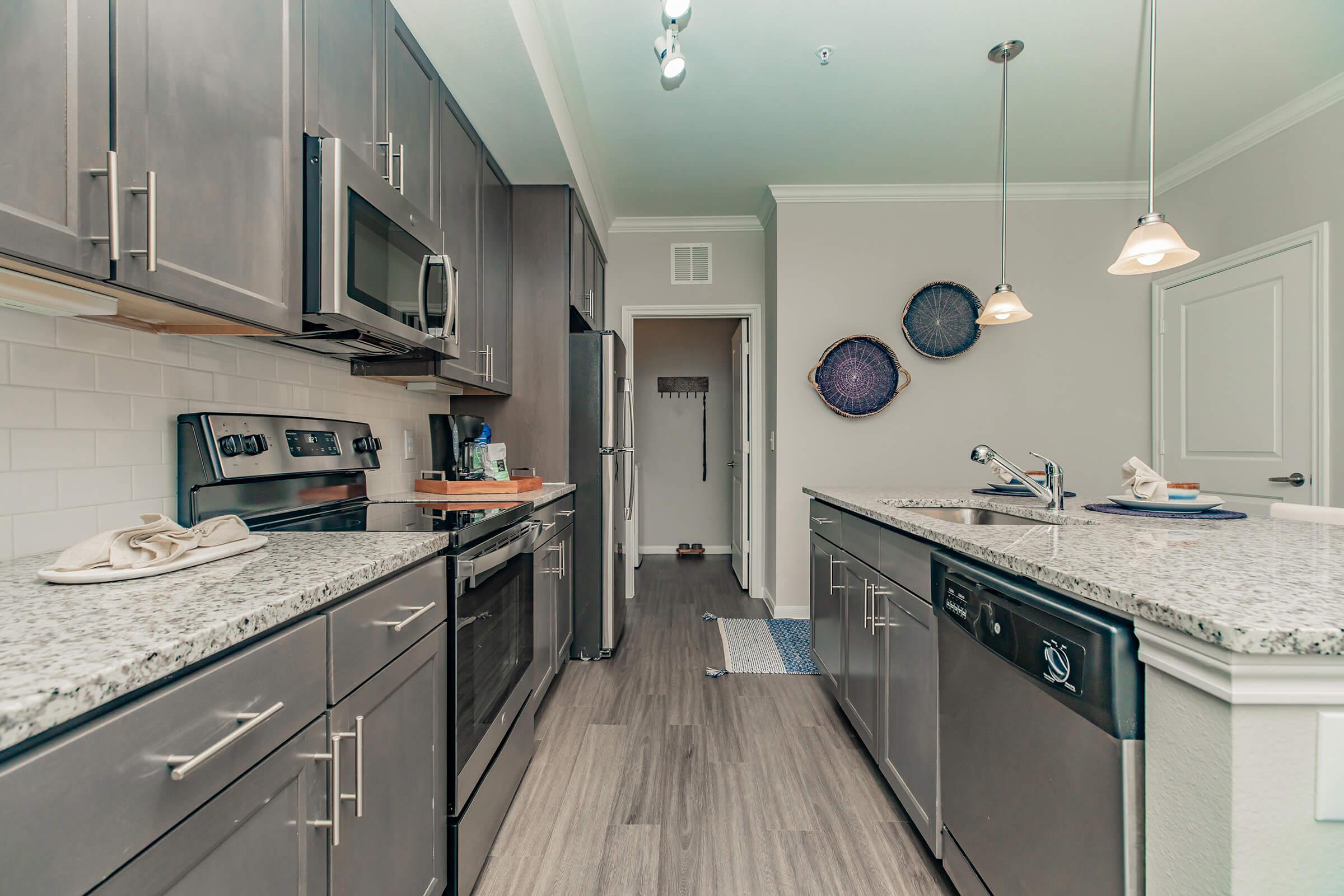 A modern kitchen featuring dark cabinetry, stainless steel appliances, and a granite countertop. There are pendant lights above the island, and a decorative wall with two circular wall hangings. The space is well-lit with natural light and has a cozy, inviting atmosphere.