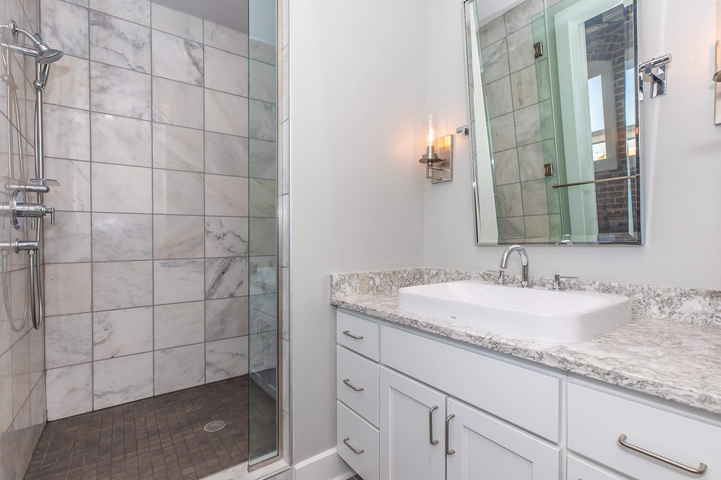 Modern bathroom featuring a glass shower with marble tiles, a sleek countertop with an undermount sink, and a large mirror. The walls are painted in a light color, enhancing the spacious feel, while stylish lighting fixtures add a touch of elegance.