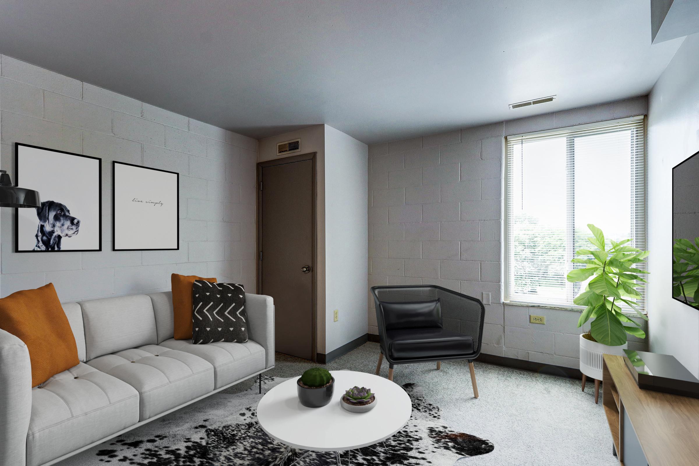 A modern living room featuring a light gray wall with two framed artworks, a comfortable white sofa with orange and black accent pillows, a sleek black chair, a round white coffee table with small plants, and large windows letting in natural light, alongside a green potted plant.