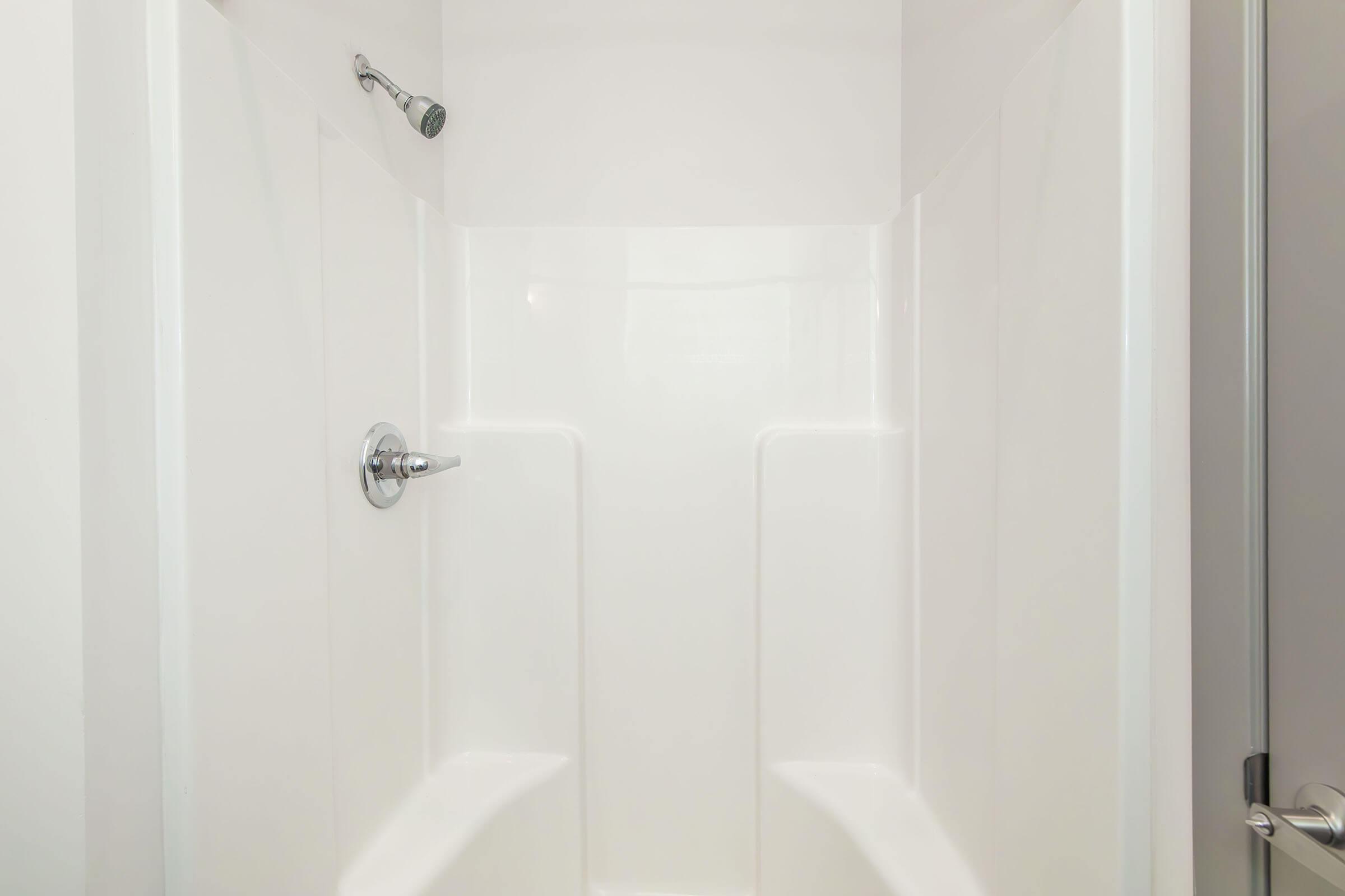 Empty and clean shower stall with smooth white walls, a handheld showerhead, and no visible fixtures or decorations. The design is modern and minimalistic, featuring built-in seating. The lighting is bright, emphasizing the cleanliness and simplicity of the space.