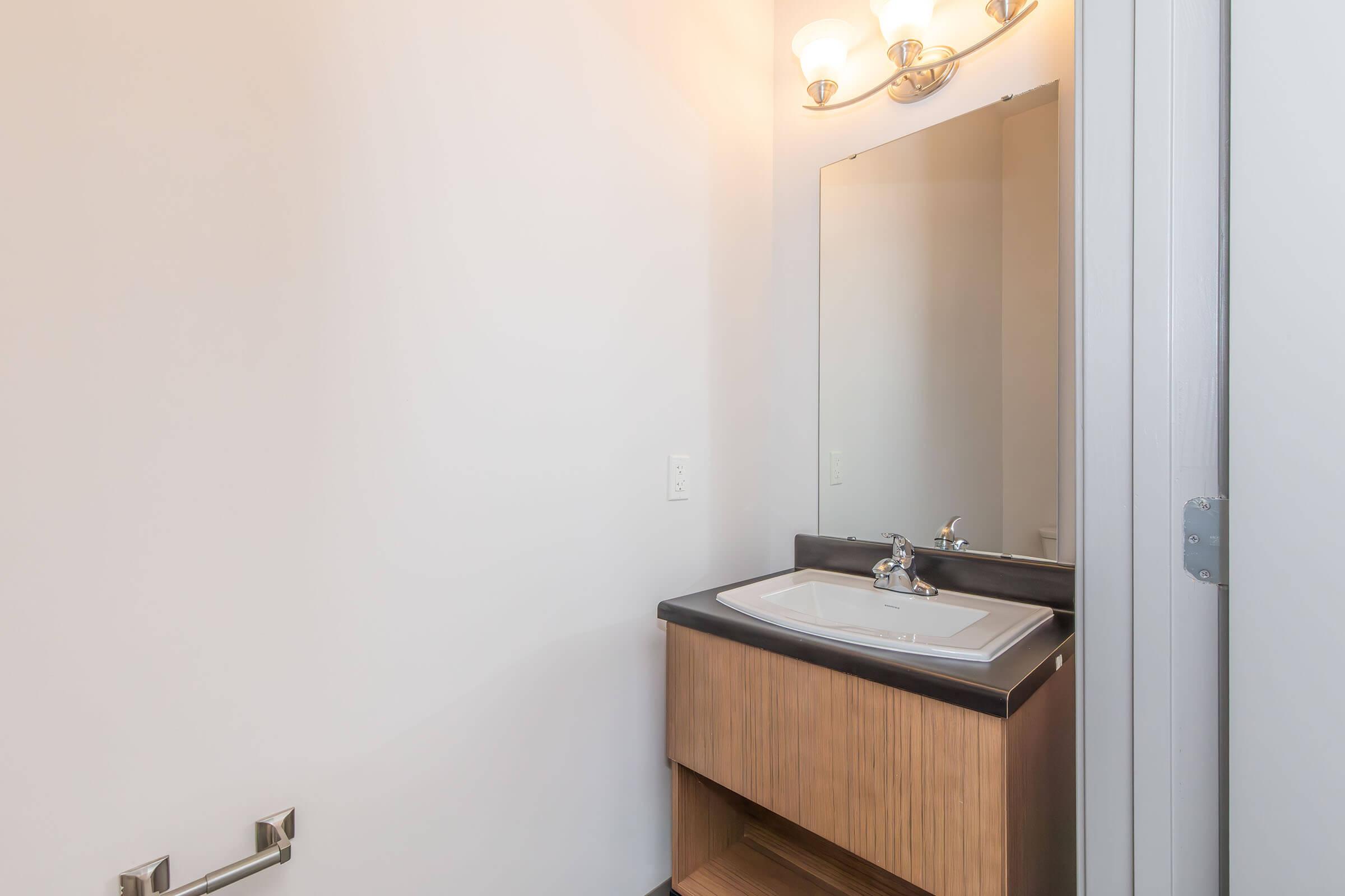 A clean and modern bathroom featuring a single sink vanity with a dark countertop, a large mirror above it, and a simple light fixture. The walls are painted in a light color, providing a bright and spacious feel. There's a towel rack beside the vanity.