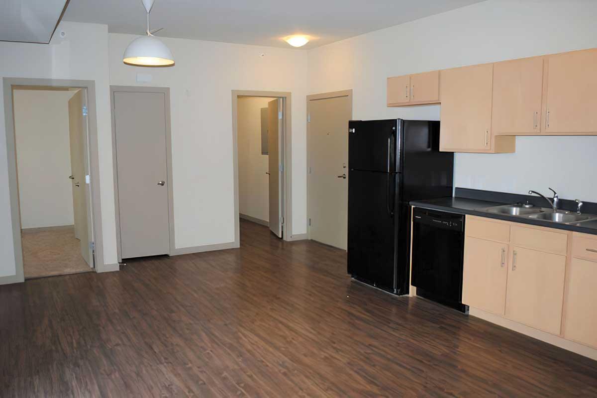 A modern kitchen area with light-colored cabinets, black appliances including a refrigerator and dishwasher, and a countertop.