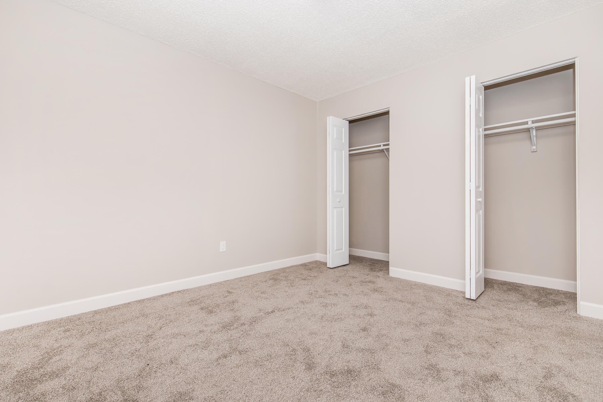 Spacious, empty room featuring neutral-colored walls and plush carpet. Two closet doors are visible on the right, providing additional storage space. The overall atmosphere is bright and clean, suitable for various decor styles.