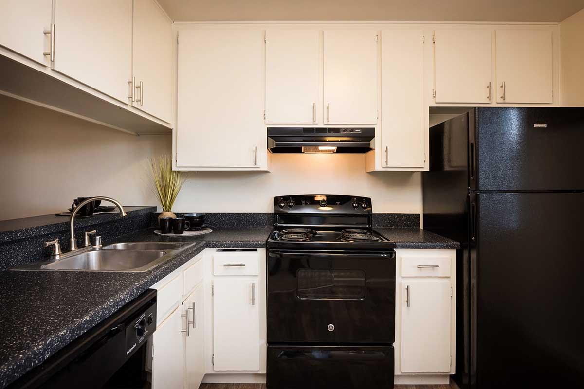 A modern kitchen featuring black appliances, including a stove and refrigerator, with white cabinets above a dark countertop. A double sink is visible, and there is soft lighting under the cabinets, creating a cozy atmosphere.
