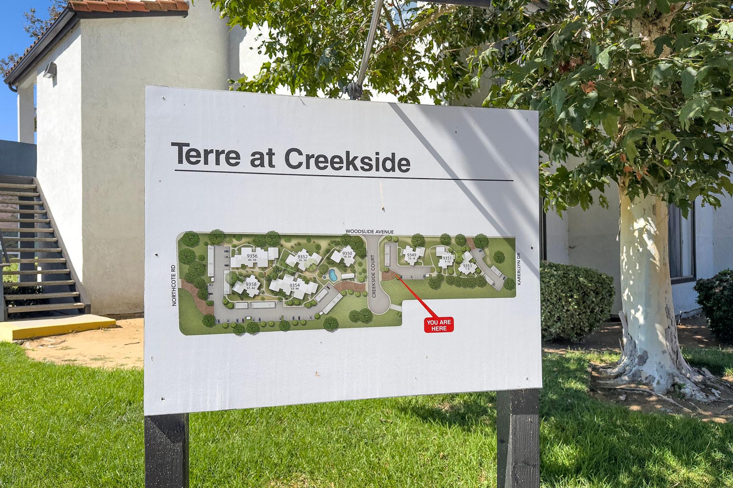 Map of the Terre at Creekside community, showing the layout of buildings and pathways. The sign indicates a marked location with "You Are Here" pointing to a specific area on the map. The background features greenery and a building.