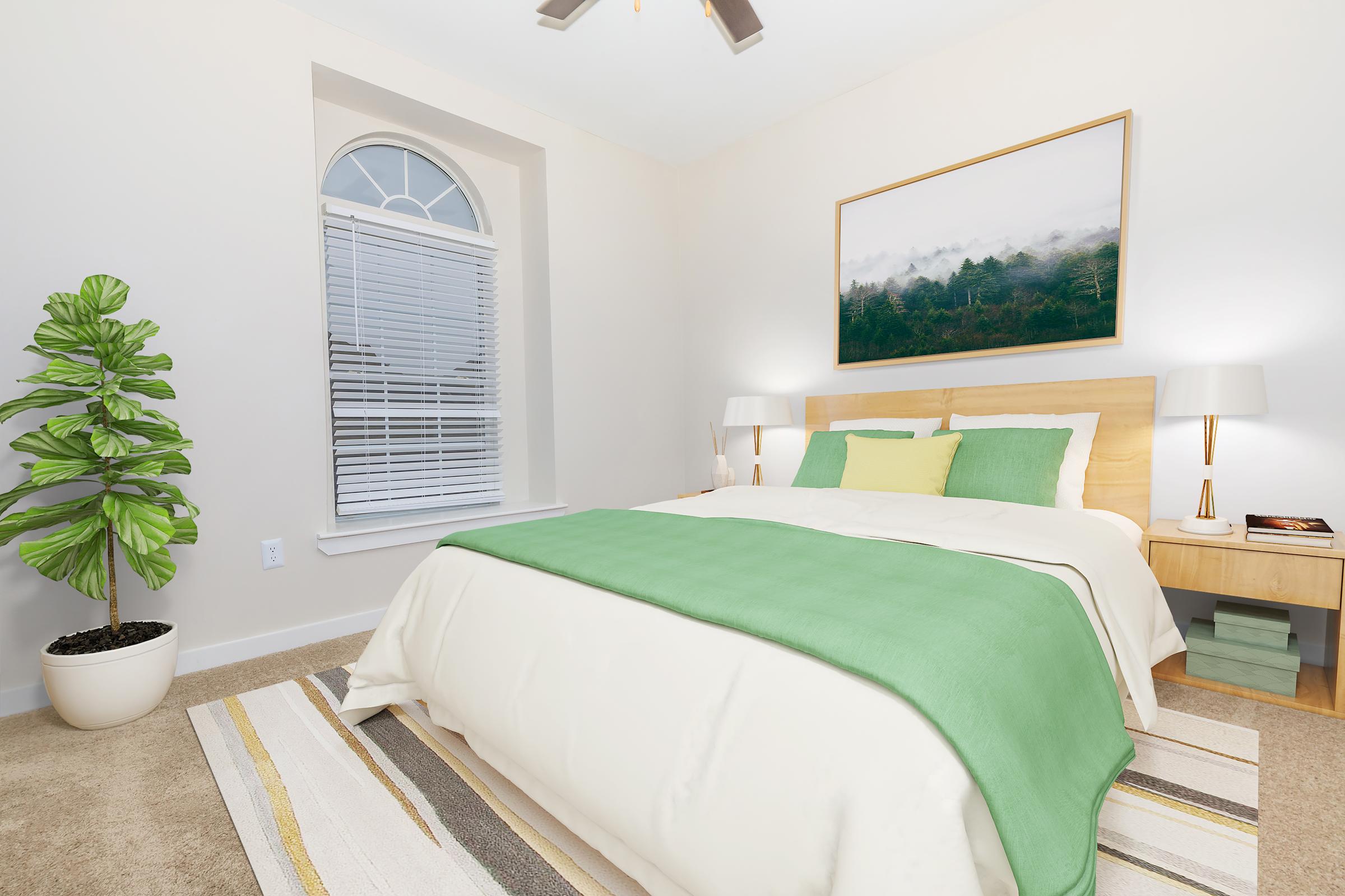 Cozy bedroom featuring a large bed with a green blanket, two bedside lamps, and a wooden nightstand. A decorative plant is in the corner, and a large framed landscape painting adorns the wall above the bed. Natural light filters through a window with white blinds.