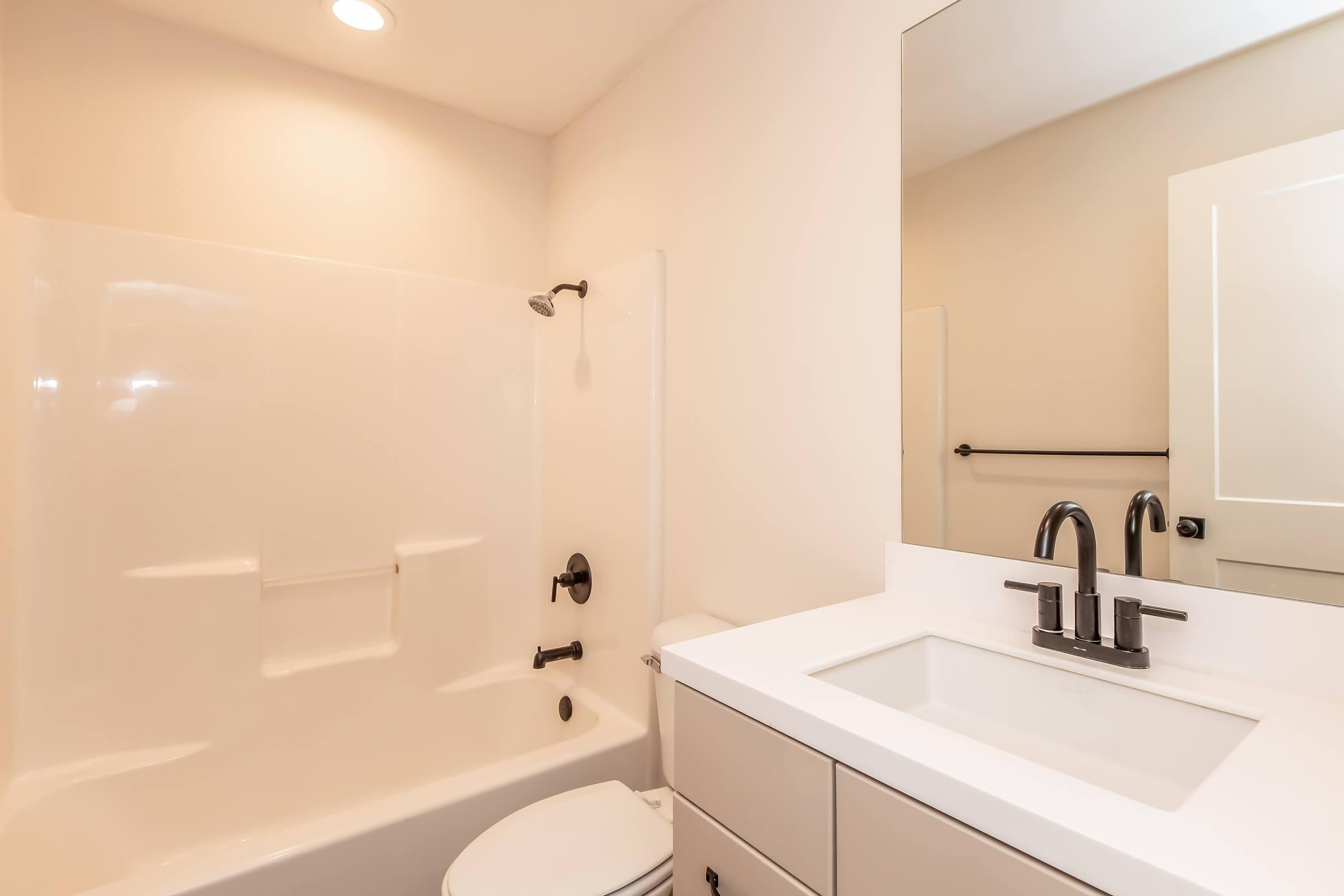A clean, modern bathroom featuring a white shower tub combo, sleek black fixtures, and a minimalist sink with a large mirror above. The walls are light-colored, and there is a simple towel bar mounted on the wall, contributing to a spacious and contemporary feel.