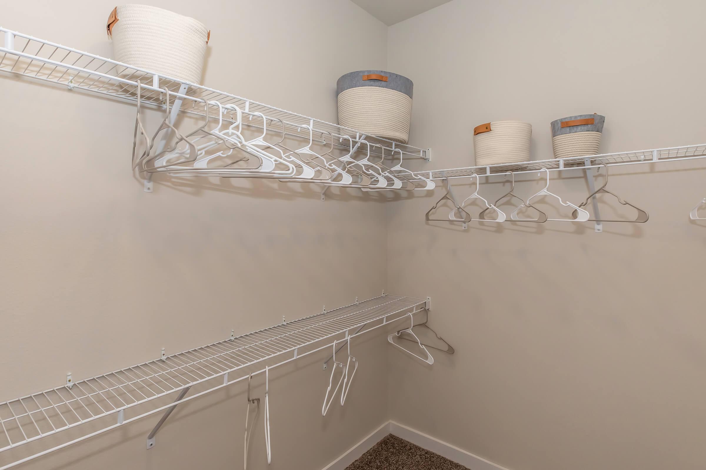 An empty closet featuring white wire shelving. The upper shelf holds several woven storage baskets, while the lower shelf has more wire hangers. The walls are painted a light color, creating a clean and organized look.