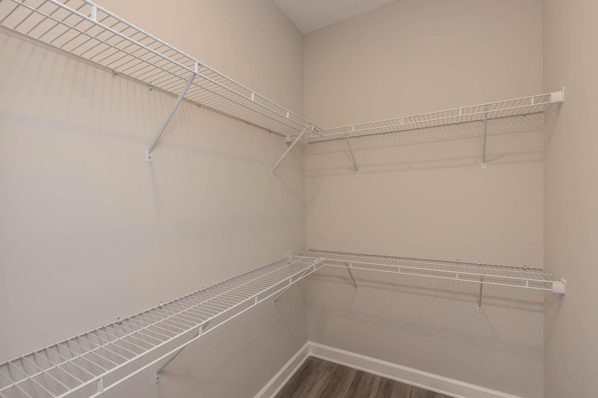 Empty closet with white wire shelving mounted on beige walls. The flooring is dark wood. The space is organized, featuring multiple horizontal shelves for storage but no items placed on them.