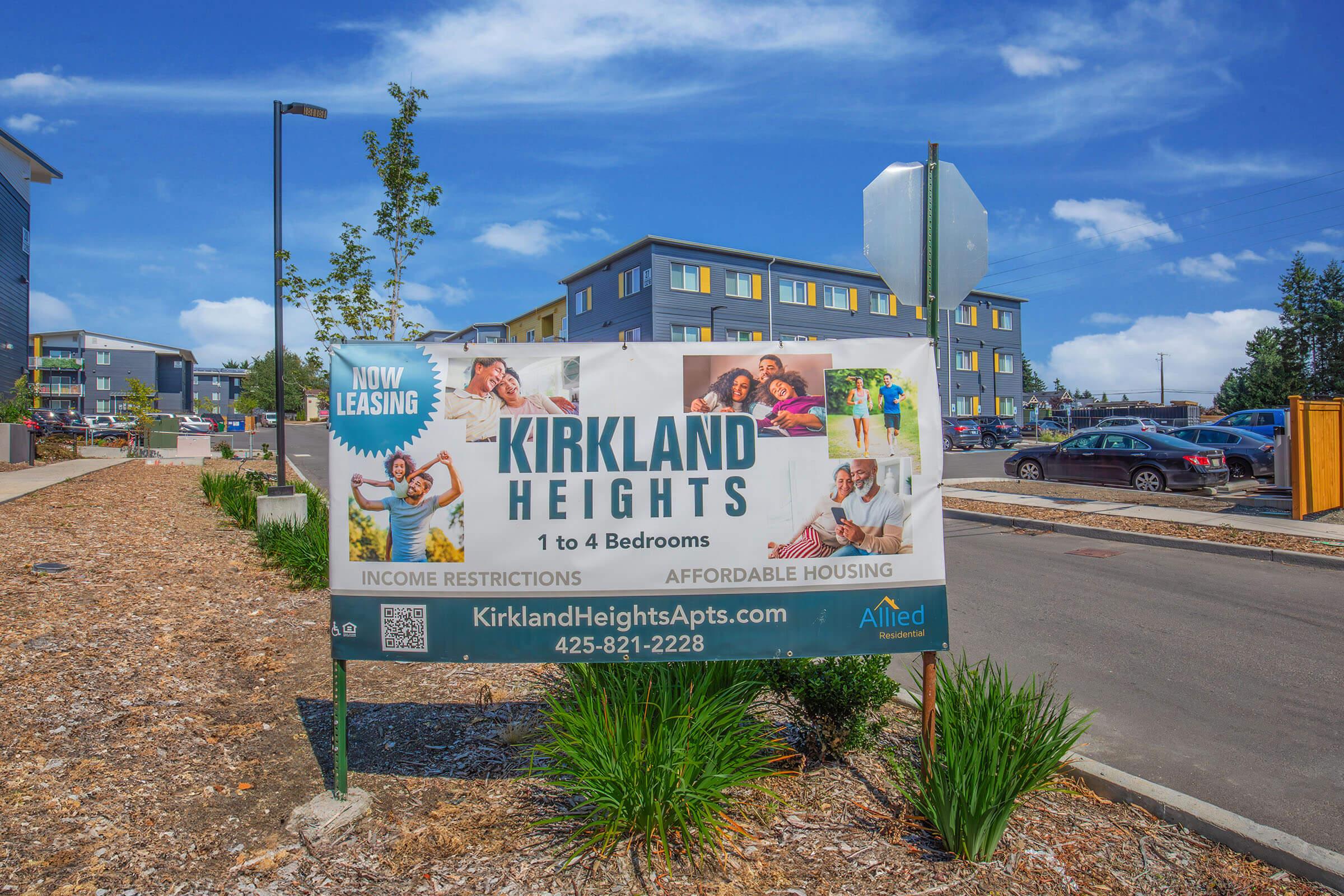 A large banner promoting Kirkland Heights apartments, featuring images of happy families. The banner indicates "Now Leasing" and mentions "Income Restrictions" and "Affordable Housing." Contact details and a website URL are also visible, along with a modern apartment building in the background.