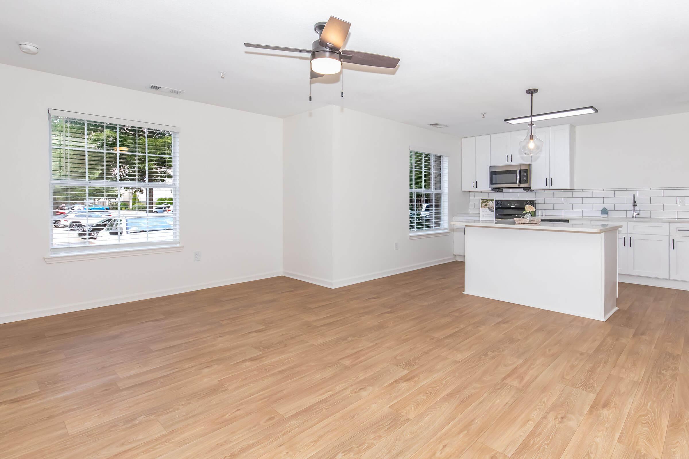 Bright and airy apartment interior featuring an open-concept living area and kitchen. The space has hardwood-style flooring, large windows allowing natural light, a ceiling fan, modern cabinetry, and stainless-steel appliances. The overall design is contemporary and inviting, perfect for comfortable living.