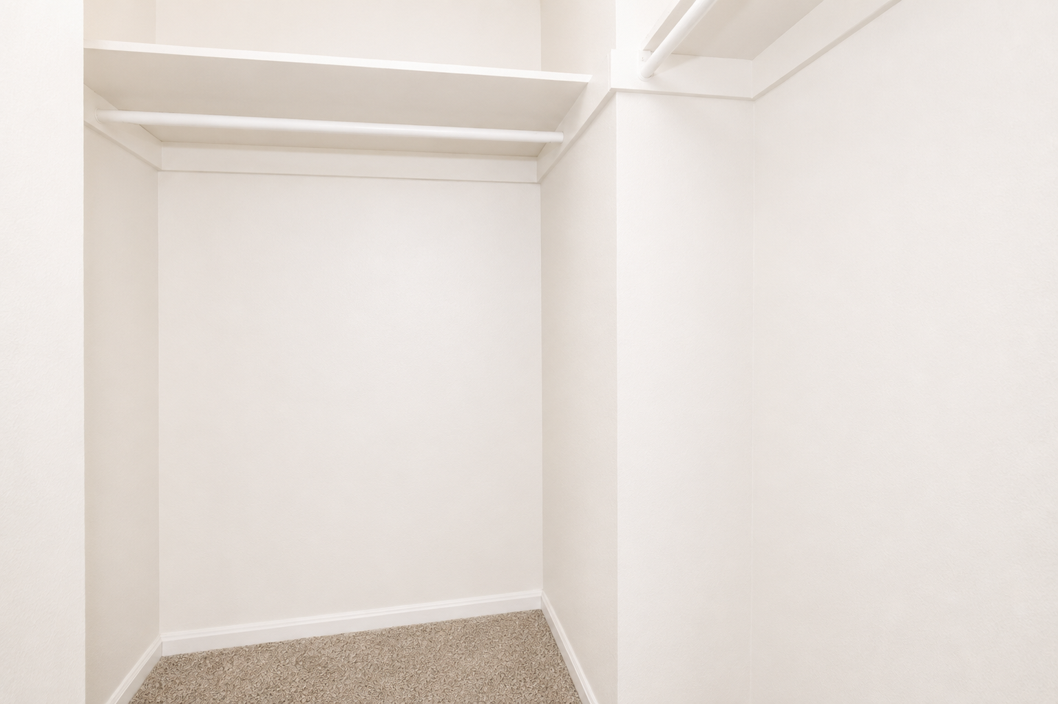 A spacious, empty closet with white walls and shelving. The floor is carpeted, and there are no items or furniture present, creating a clean and minimalist appearance.