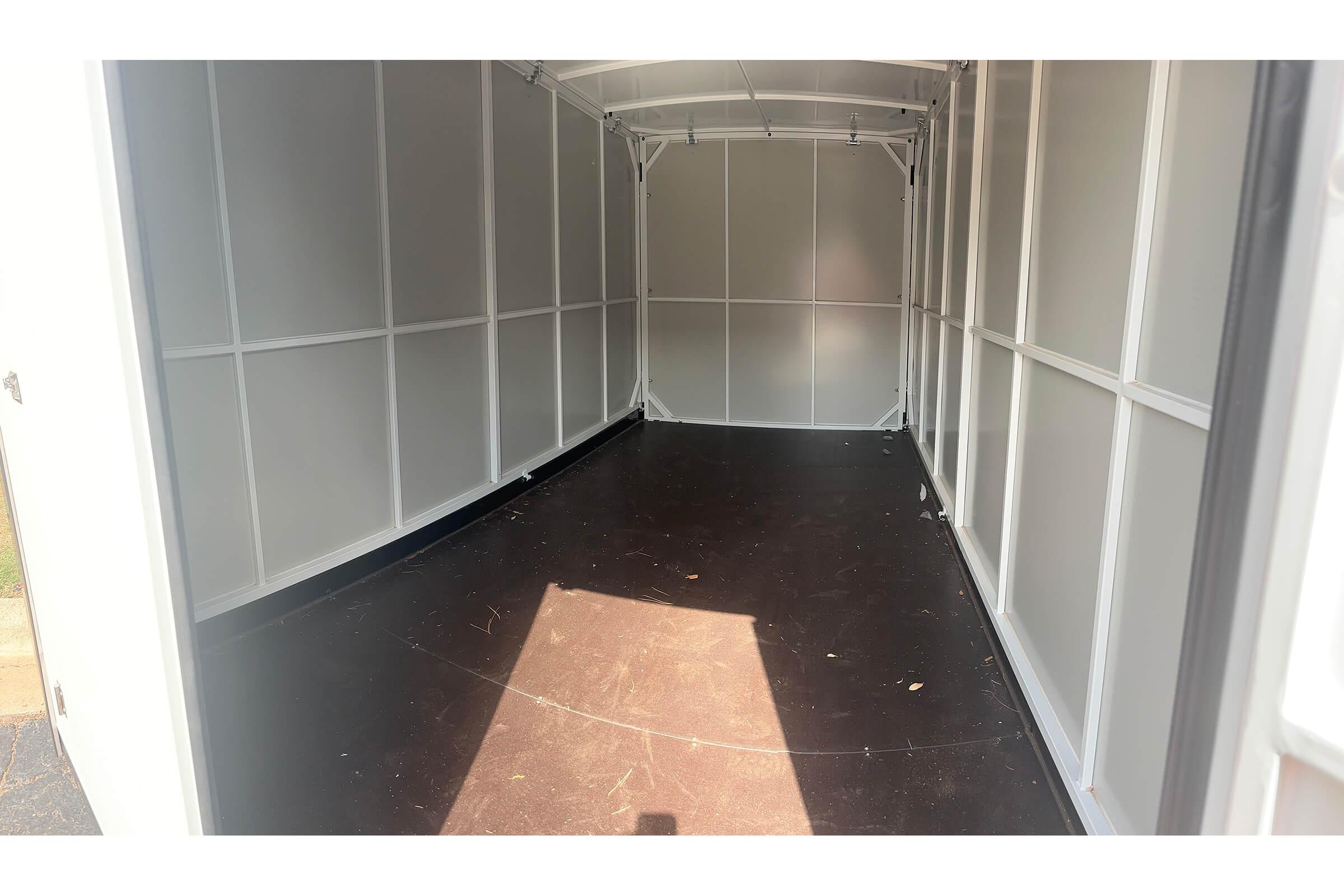 Interior view of an empty storage trailer with white walls and a dark floor. The trailer is well-lit with sunlight coming from the entrance, highlighting the spacious and uncluttered area.