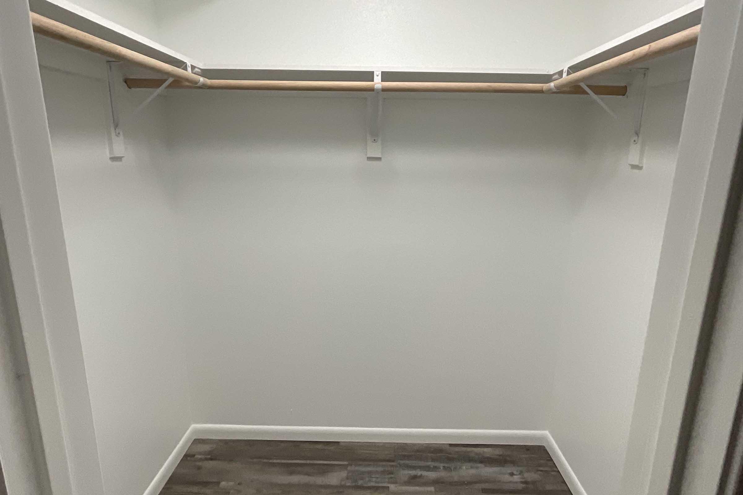 Empty closet with white walls and a light gray floor. Two wooden rods for hanging clothes are mounted on the walls, and there are no shelves or items inside. The space is clean and organized, creating a minimalist look.