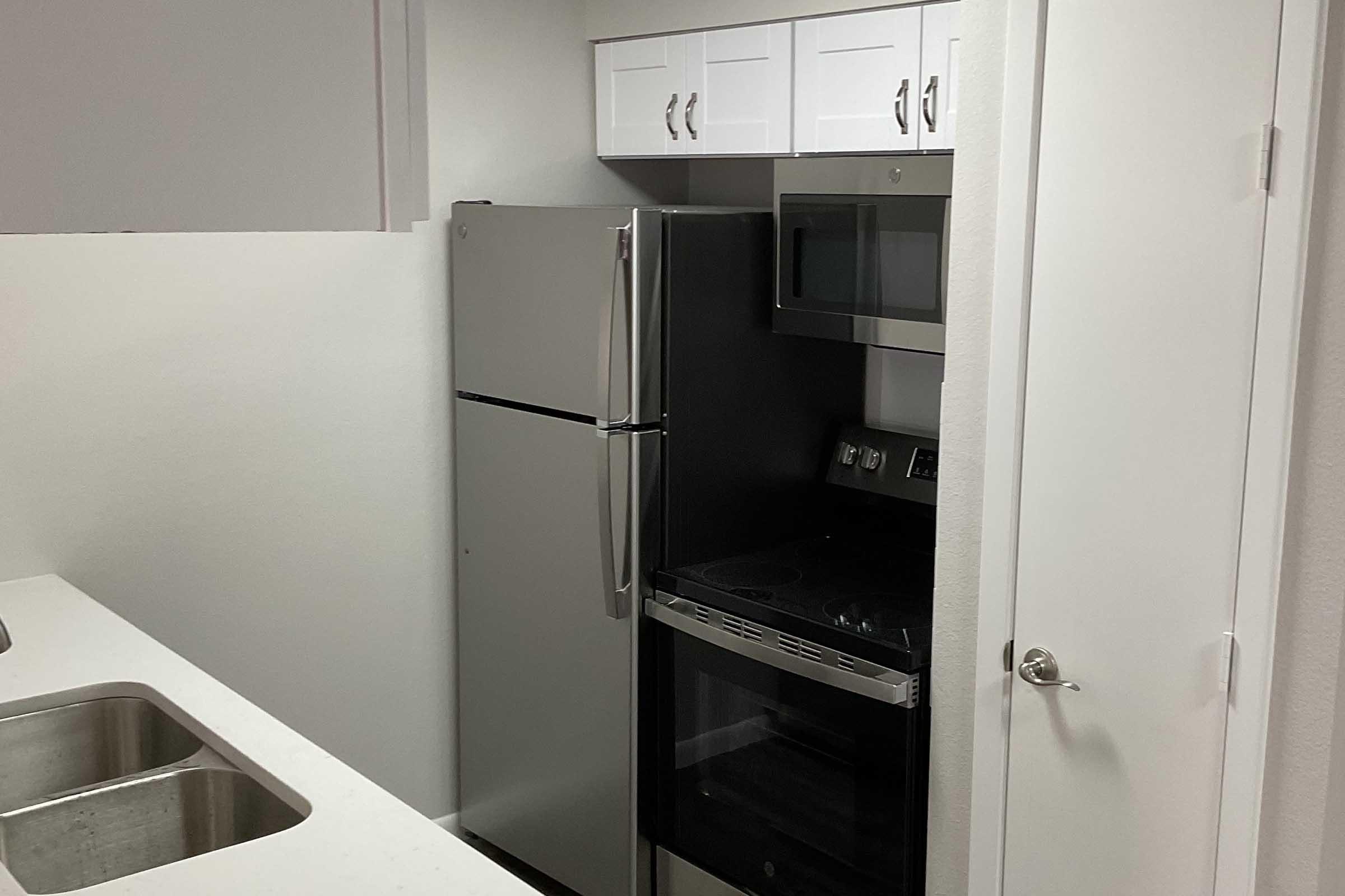A modern kitchen featuring stainless steel appliances, including a refrigerator, microwave, and oven. The cabinetry above the appliances is white, and the countertop is a light color. The kitchen has a clean, minimalist design with an emphasis on functionality.