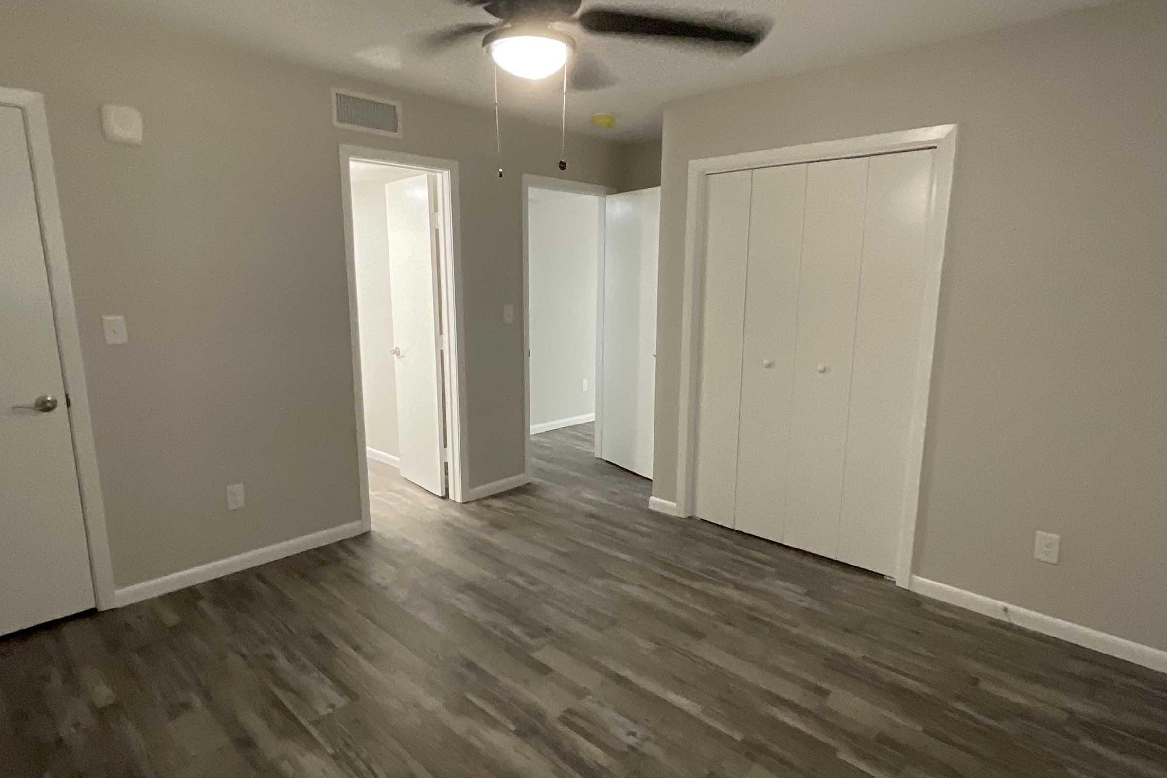 A well-lit interior room with a ceiling fan, featuring light gray walls and laminate flooring. Two doorways lead to other rooms, and there are two white closets with double doors. The space is clean and organized, creating a comfortable atmosphere.