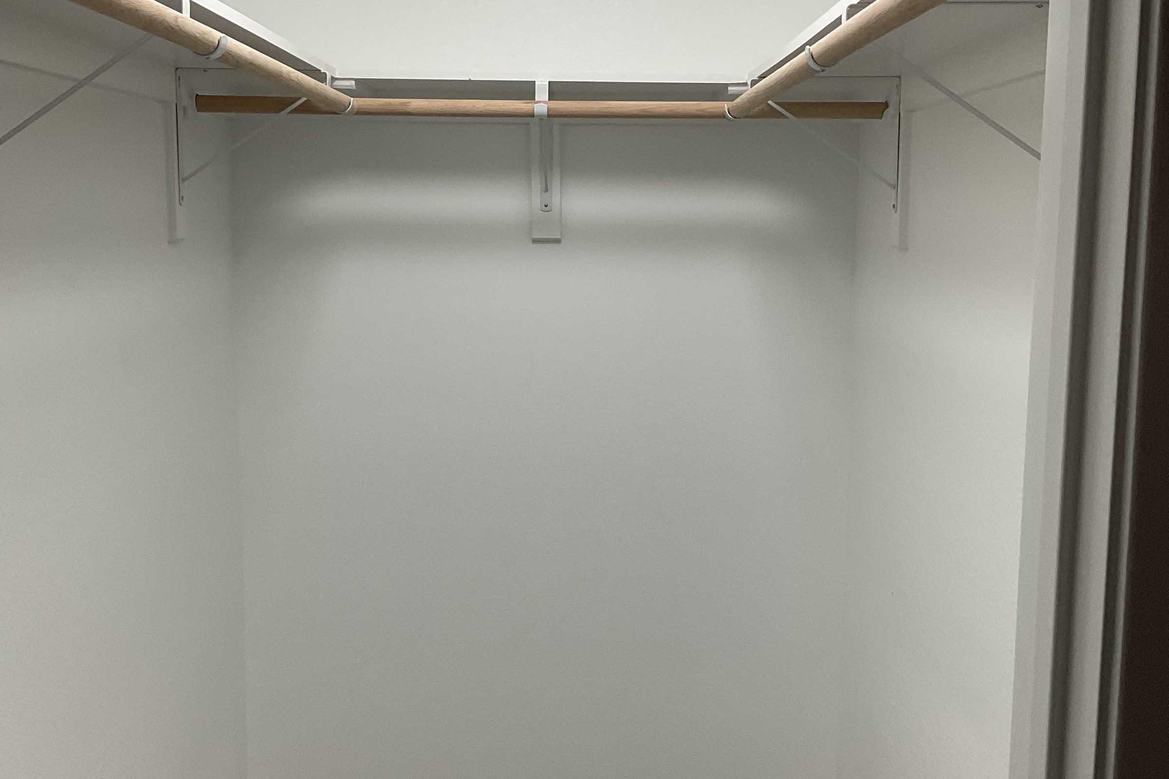 A minimalist closet with two wooden hanging rods on white walls. The space is empty, featuring a clean and organized look, with no items or shelving visible.