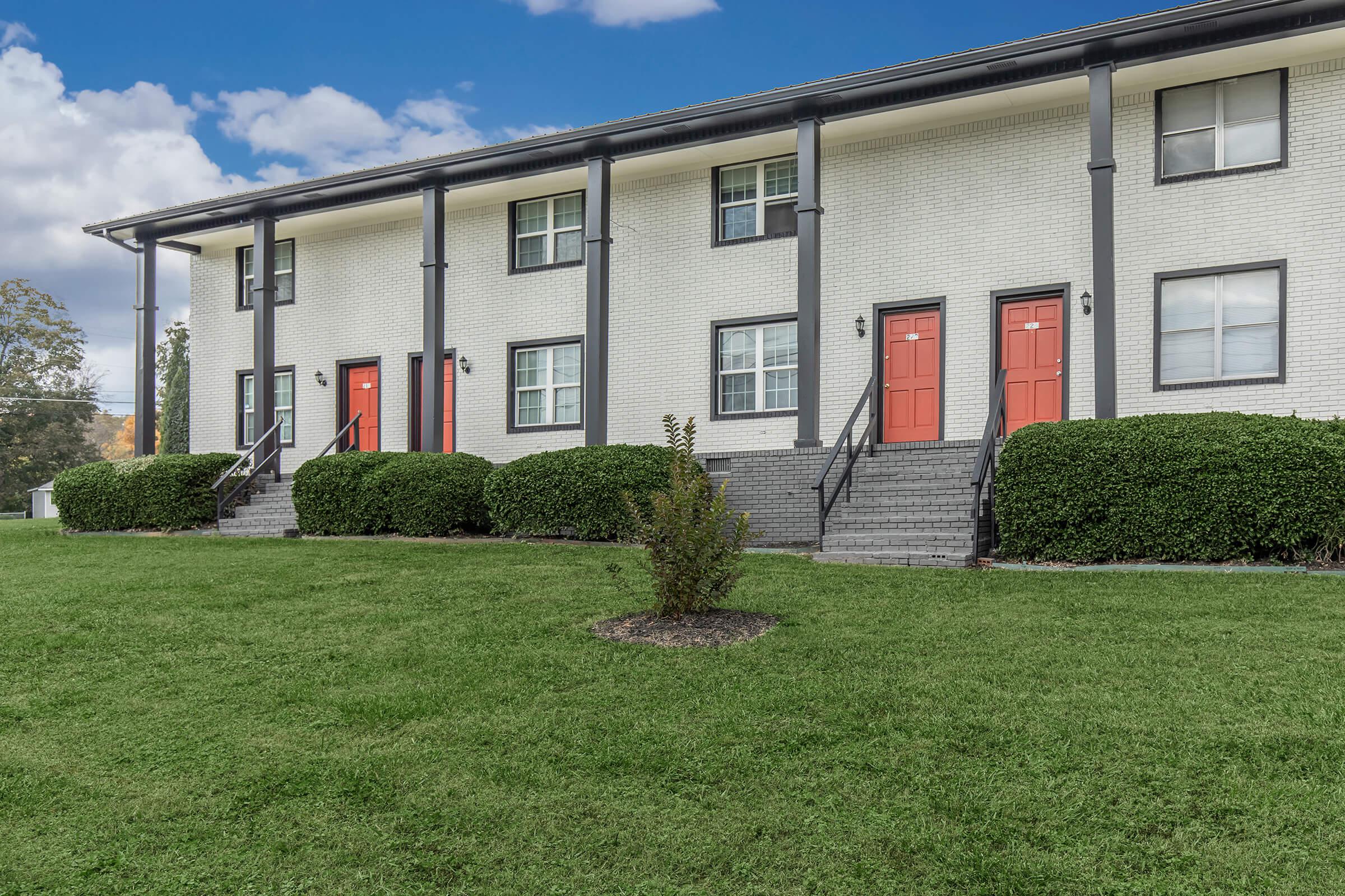 Another view of Elements44 Townhomes beautifully landscaped townhomes showing four homes with orange front doors, white brick exterior, and eight windows