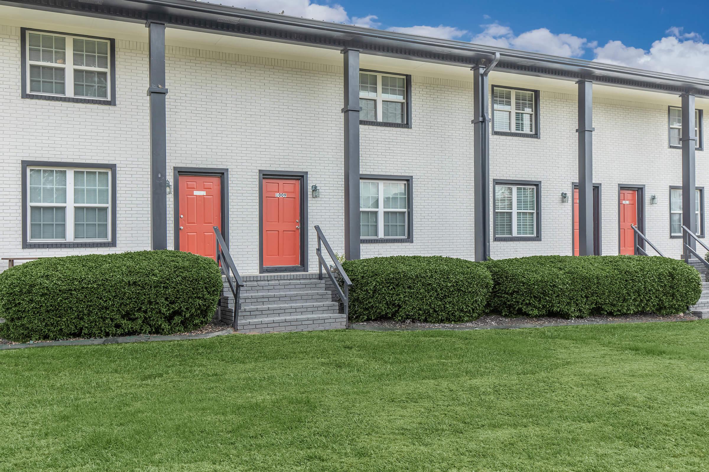 The Elements44 Townhomes brick walls with the orange doors and black pillars with the green grass and bushes