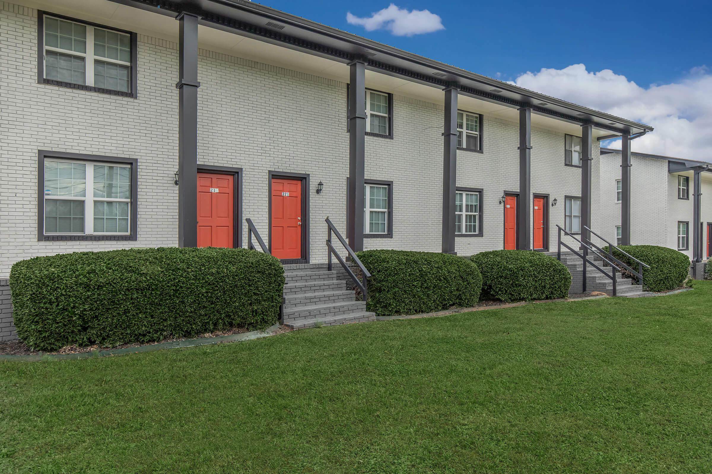 The Elements44 Townhomes showcases beautifully landscaped lawns with green grass, bushes, and the orange doors with the brick homes