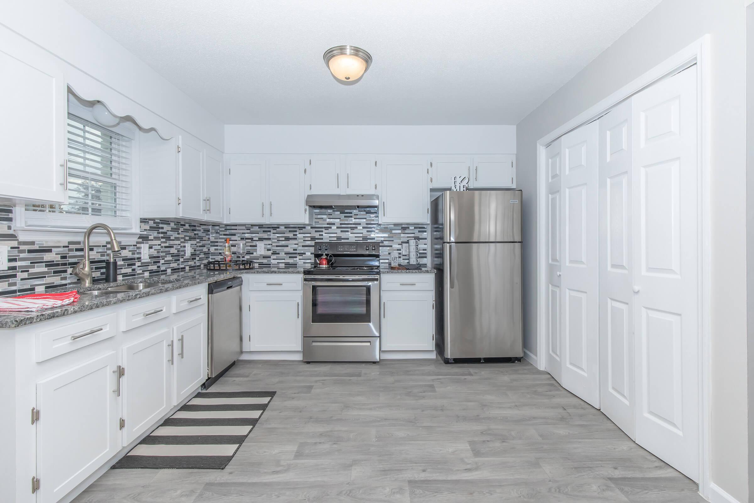 The Elements44 Townhomes kitchen with stainless steel appliances, hardwood floors, white cabinets, and file backsplashes