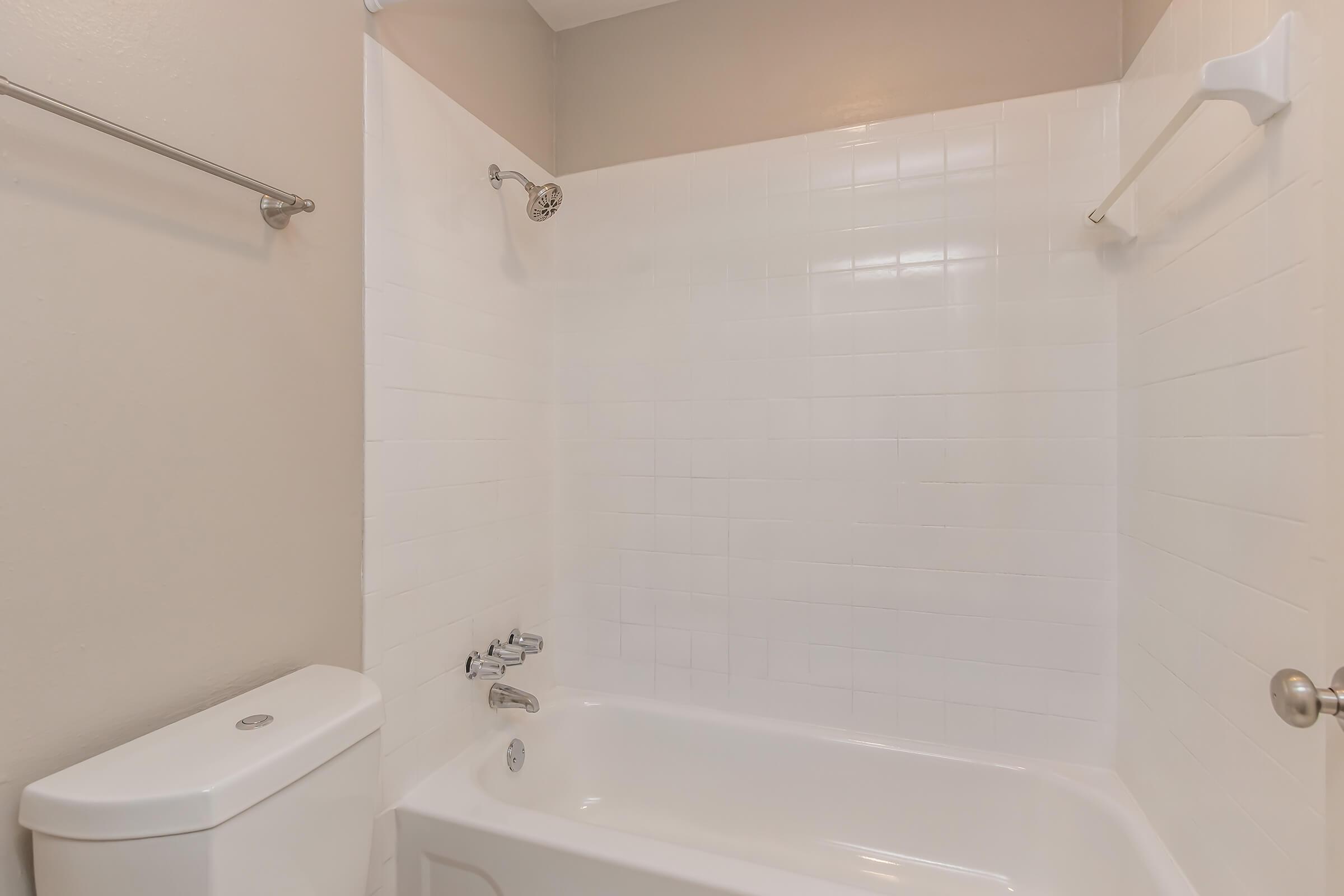 Clean bathroom featuring a white tiled shower and bathtub combination. A toilet is positioned to the left, and there are shower fixtures on the wall. The overall space has neutral-colored walls and a well-maintained appearance.