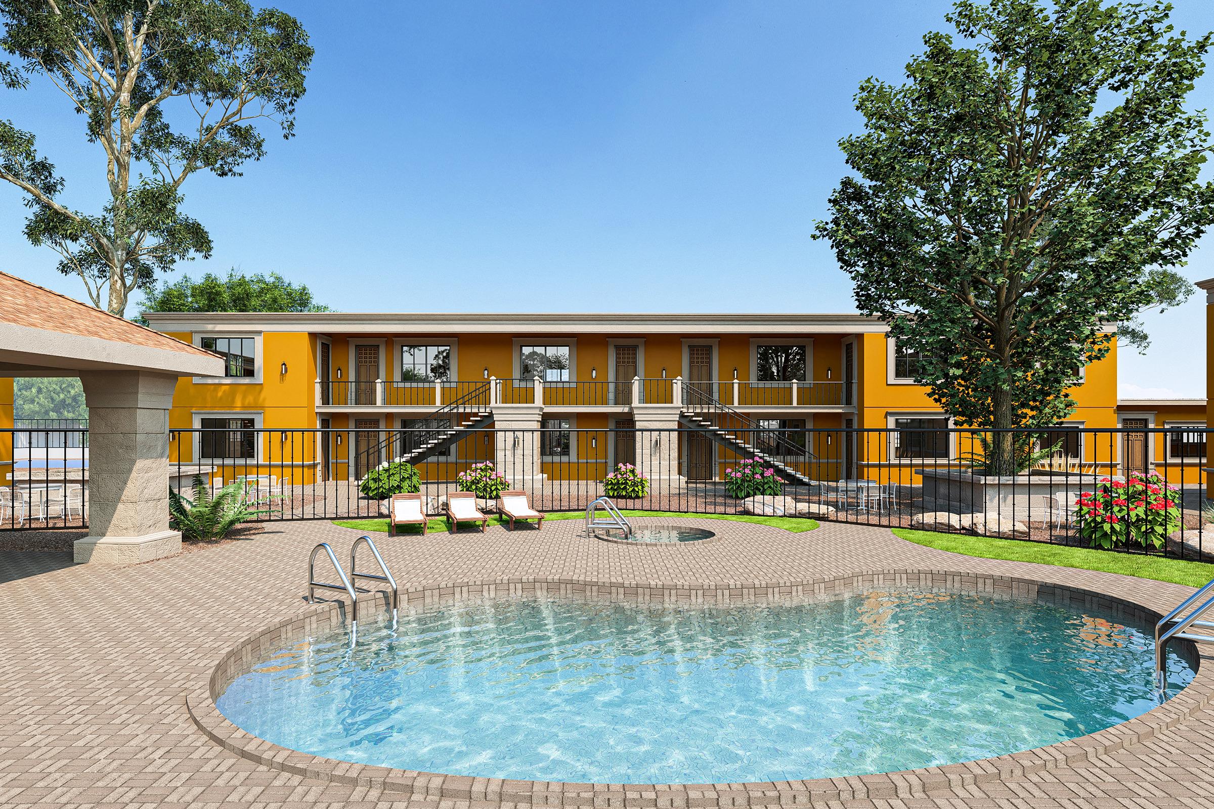 A vibrant outdoor area featuring a swimming pool with lounge chairs, surrounded by landscaped greenery. In the background, a two-story building with a bright yellow facade can be seen, along with a fenced enclosure that highlights the inviting atmosphere of the space.