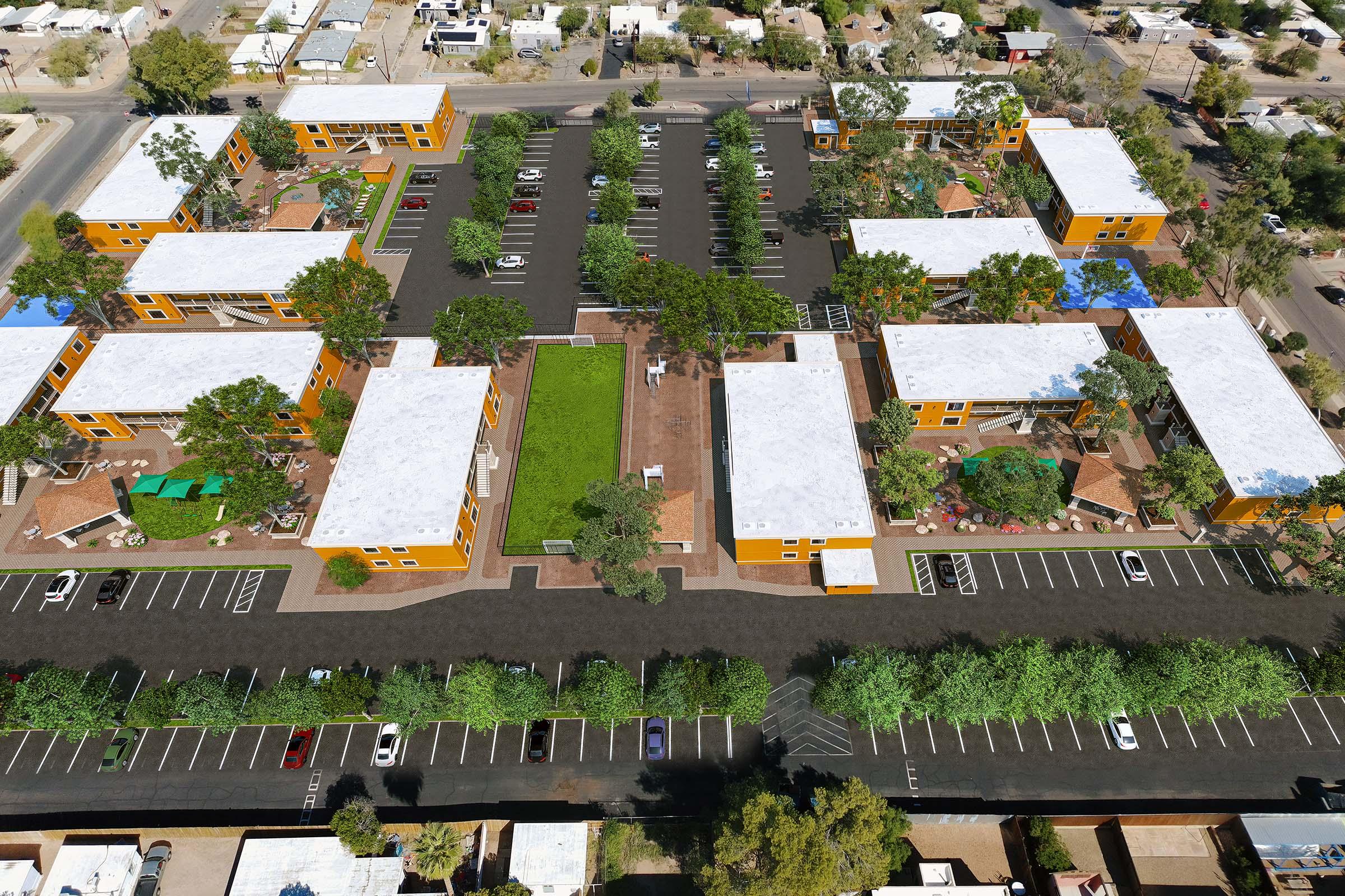 Aerial view of a residential complex featuring multiple yellow buildings with white roofs. The area includes landscaped green spaces, parking lots filled with cars, and communal areas with seating. Surrounding the complex are trees and pathways, creating a vibrant and inviting community atmosphere.