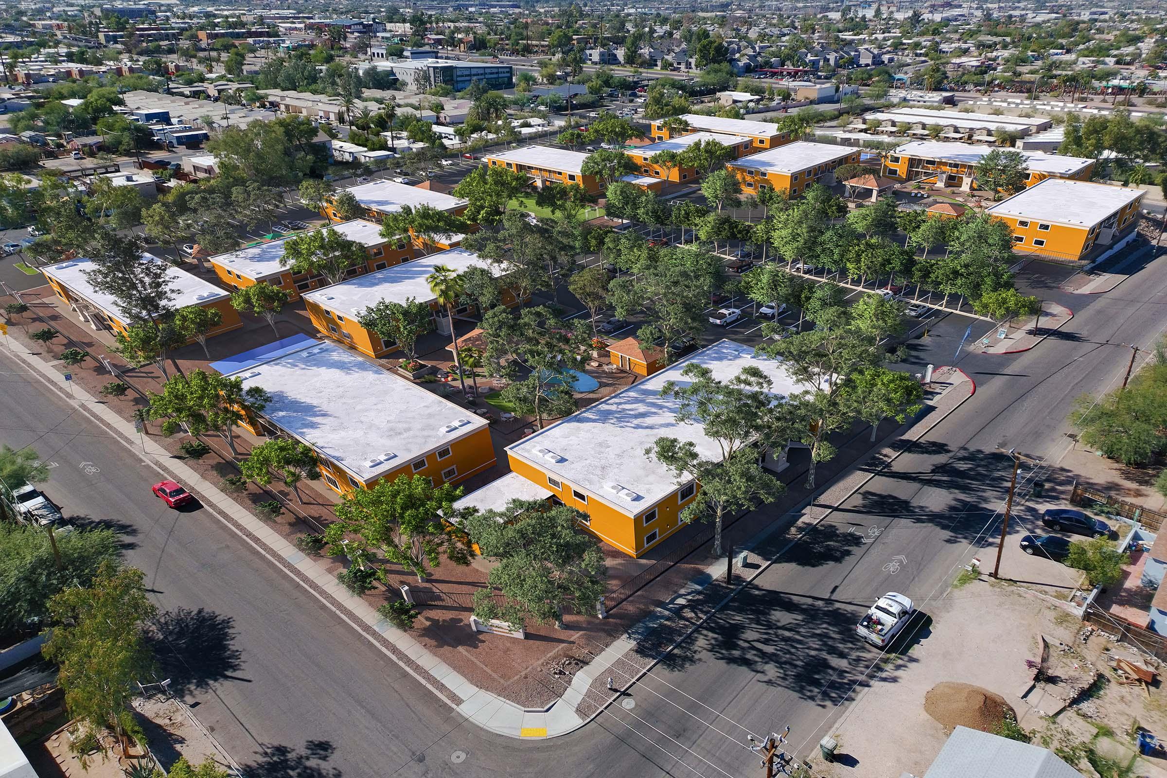 Aerial view of a residential neighborhood featuring several orange apartment buildings surrounded by trees. The area includes landscaped pathways and parking lots, with streets visible at the edges. Nearby, there are additional buildings and an urban landscape in the background.