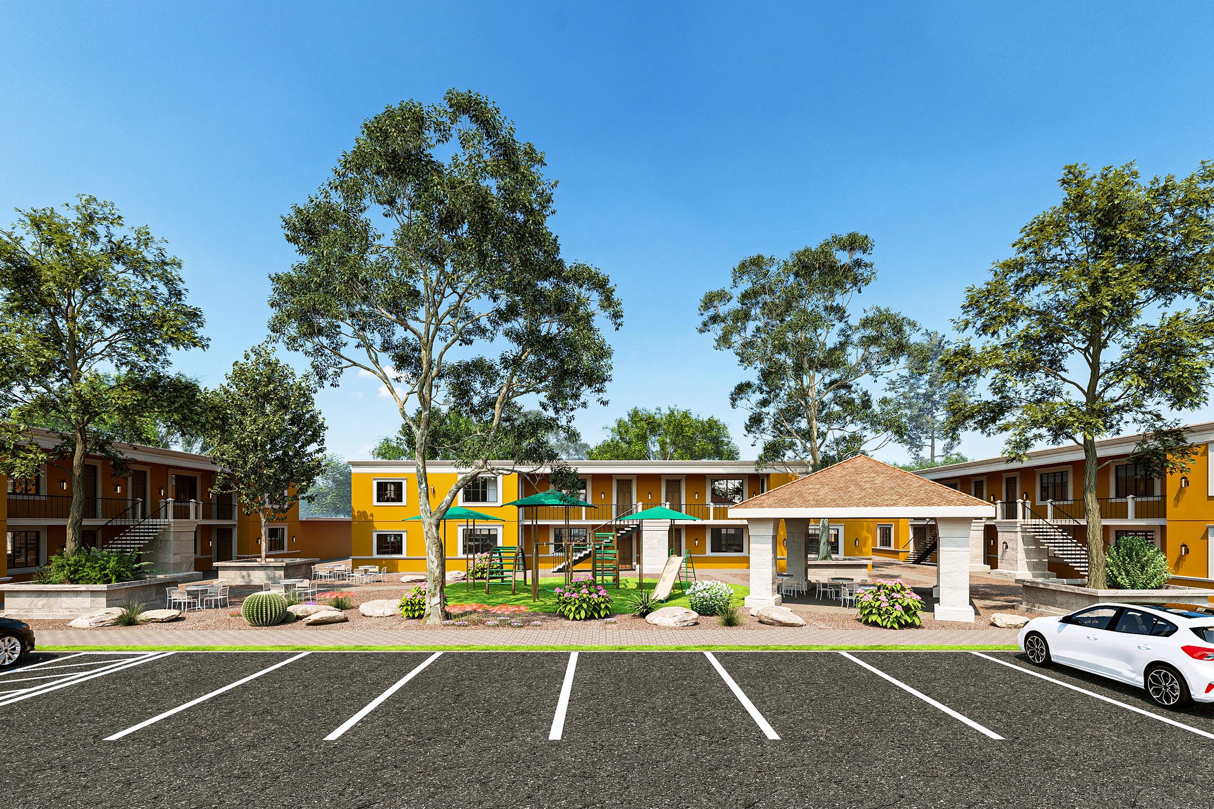 A sunny outdoor view of a residential complex featuring two-story buildings in warm yellow hues. In the foreground, there is a parking area with marked spaces. Centered is a playground surrounded by greenery, with trees providing shade. A gazebo is visible, adding to the inviting atmosphere.