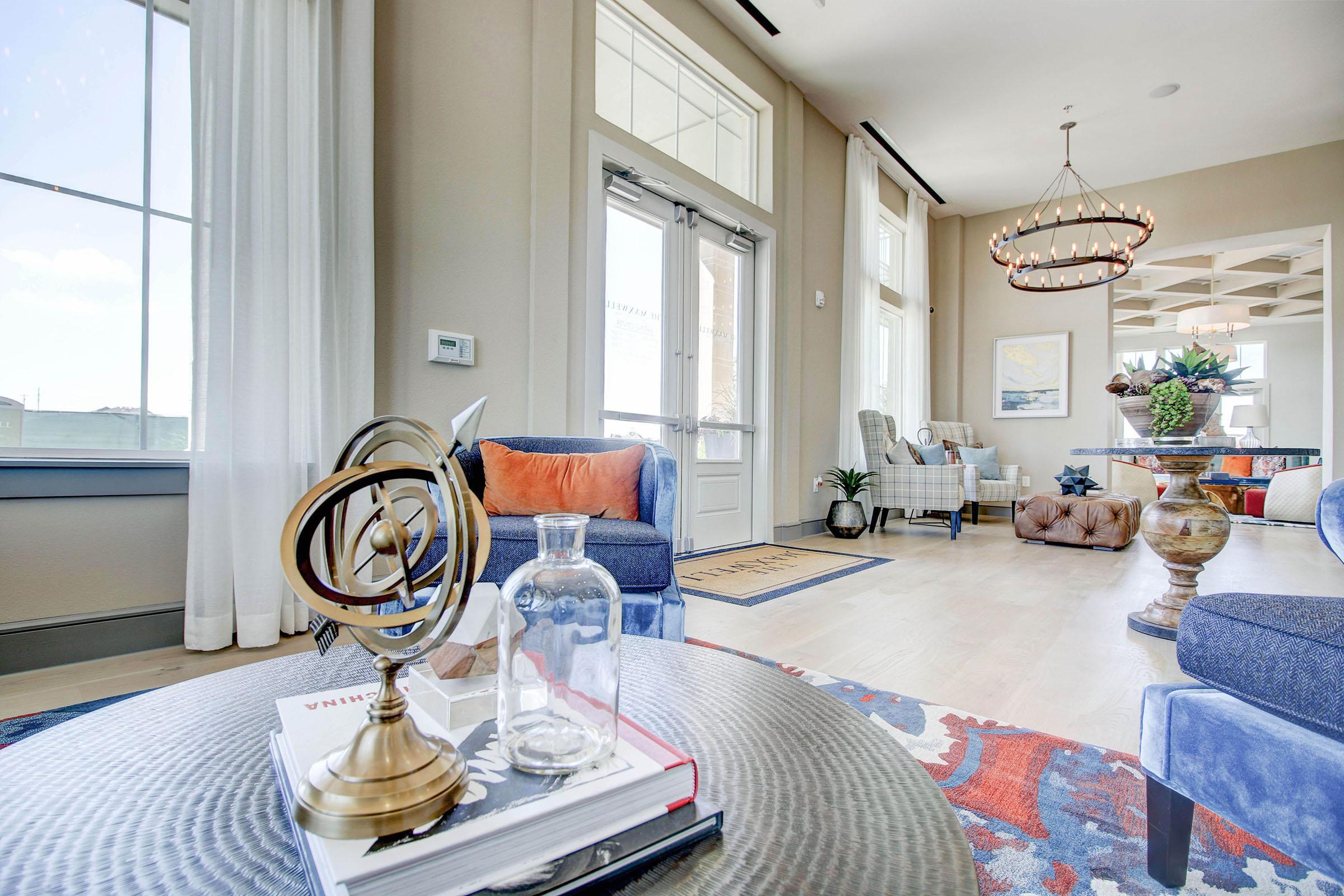 A stylish living room featuring comfortable armchairs, a coffee table with decorative items, large windows letting in natural light, and a modern chandelier. A cozy atmosphere is created with a mix of textures and warm colors, enhancing the inviting space.