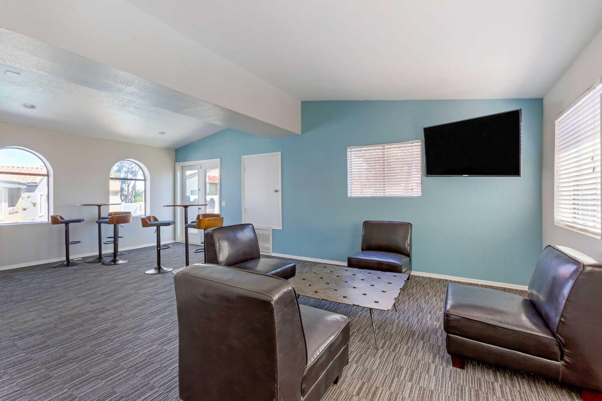 A modern lounge area featuring two black chairs and a black ottoman on a gray carpet.