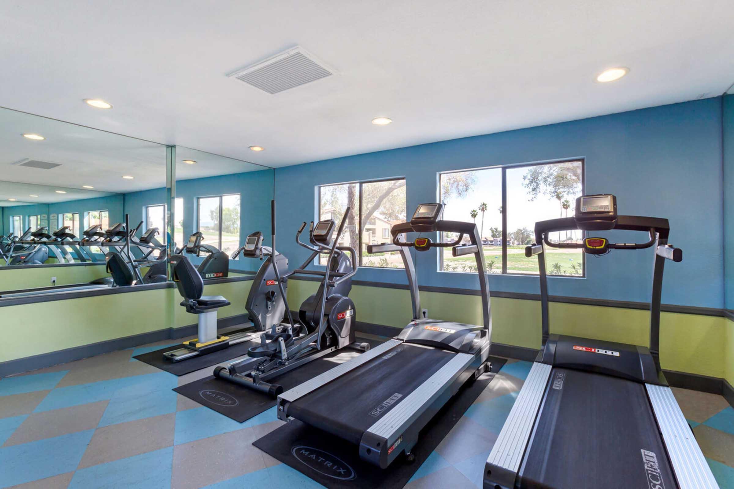 A bright and modern gym featuring multiple treadmills, an elliptical trainer, and a stationary bike.