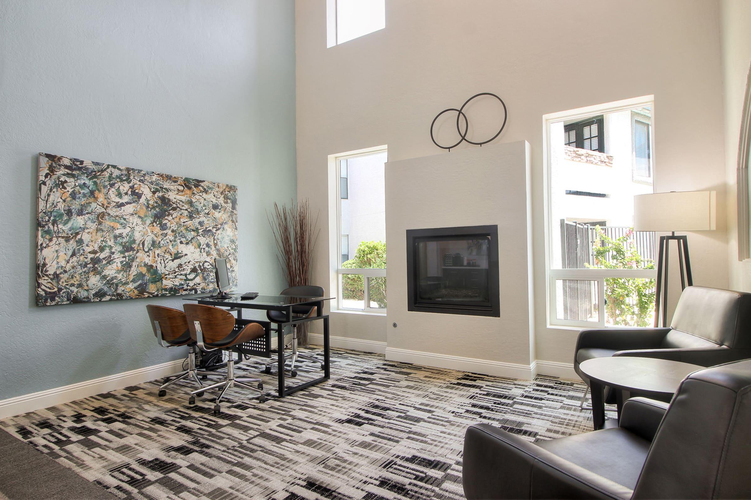 A modern living space featuring a large abstract painting on the wall, a small desk with two wooden chairs, and a stylish black seating area.
