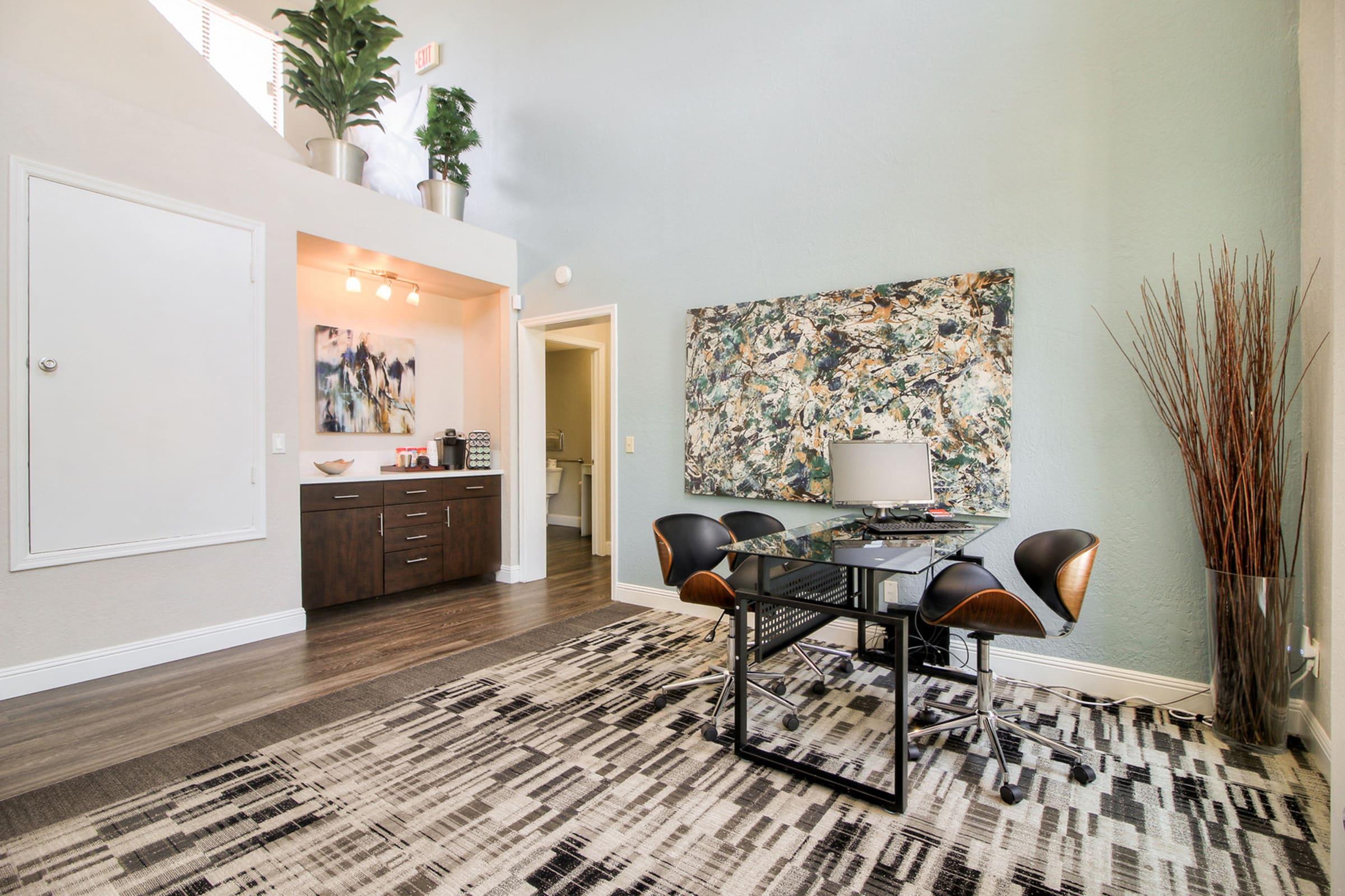 Modern interior view of a spacious room featuring a glass-top desk with black chairs, a large abstract wall art piece, and a cozy area rug.