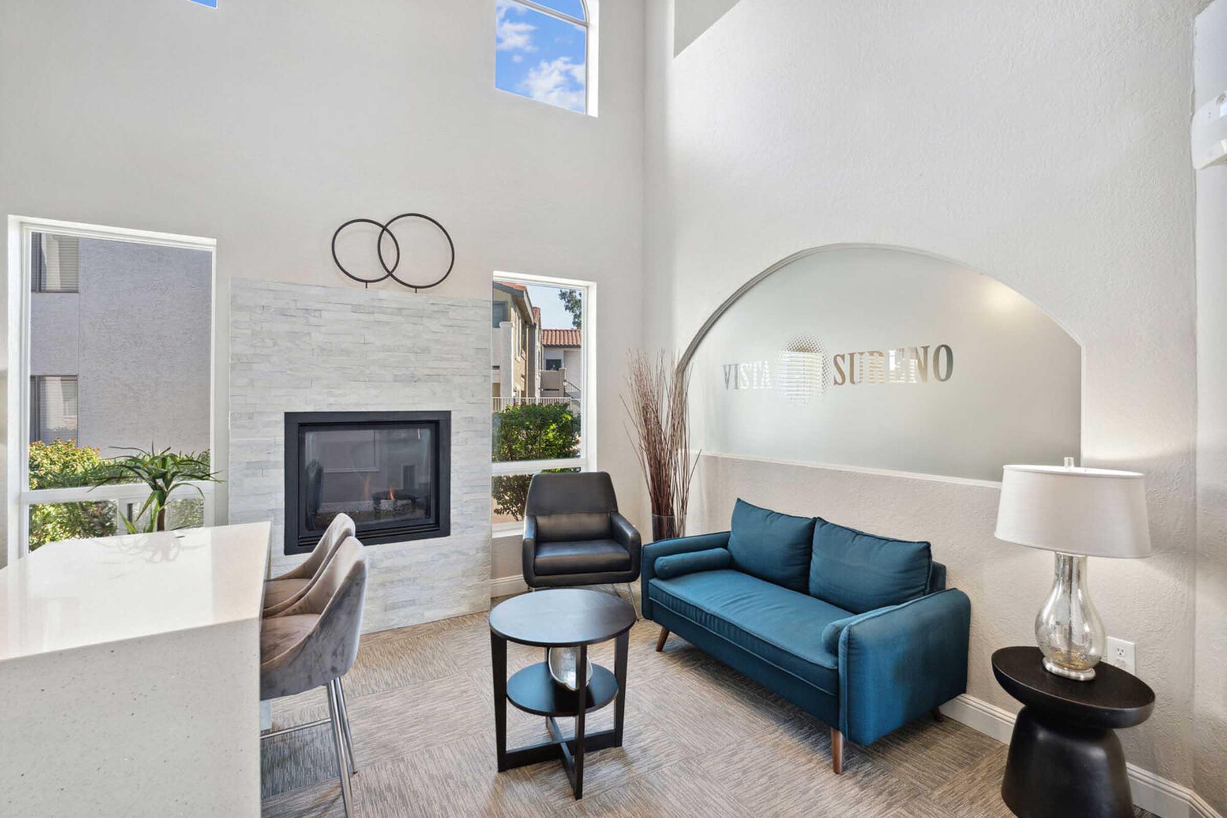 Modern living room with large windows allowing natural light, featuring a blue sofa, a black armchair, and a small round table.