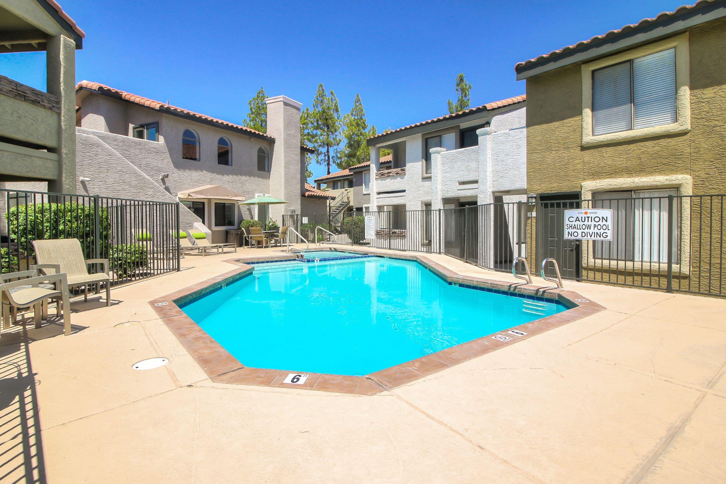 A clear blue swimming pool surrounded by a gated area, with lounge chairs around it.