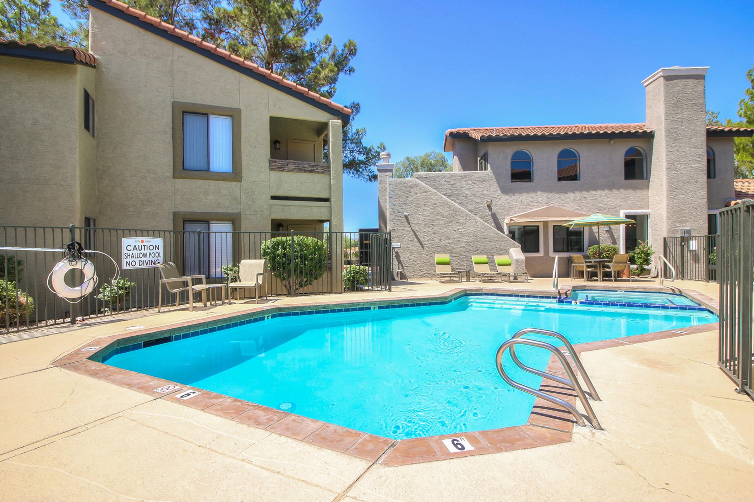 A clear blue swimming pool surrounded by a fenced area, with lounge chairs on the pool deck.