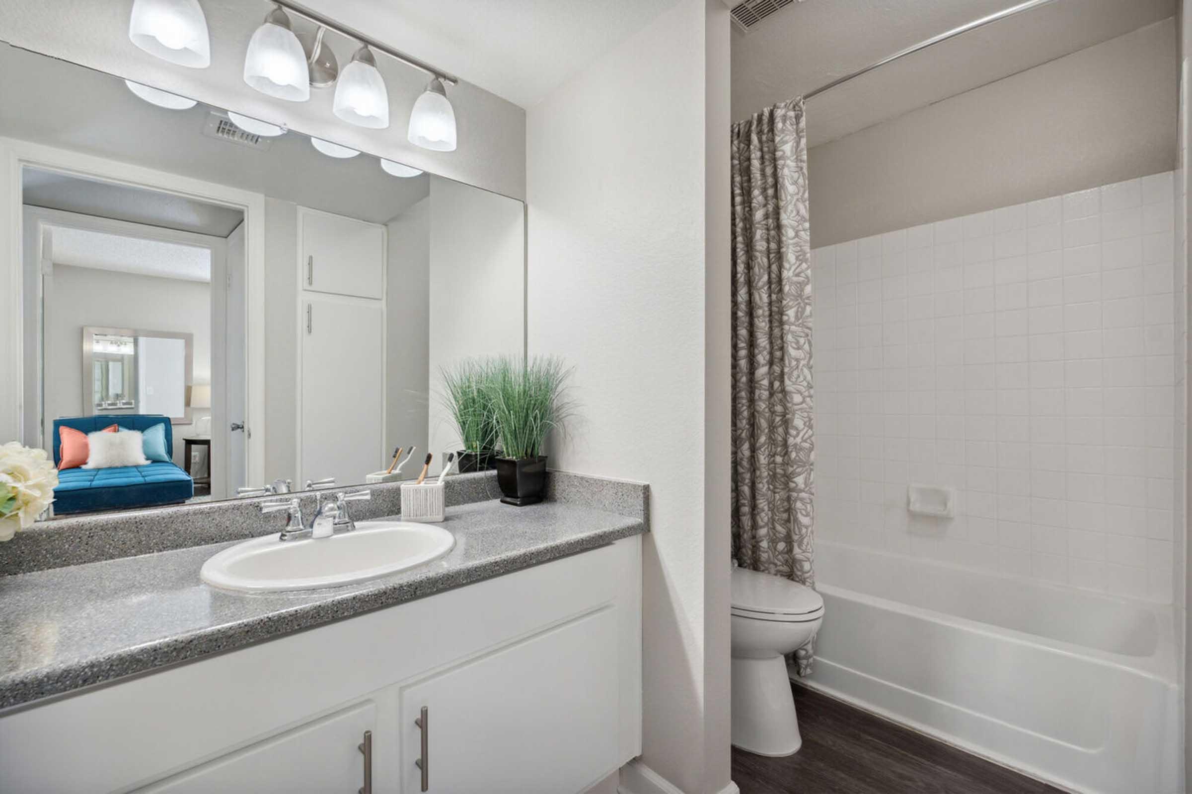 A modern bathroom featuring a granite countertop with a sink, a large mirror, and overhead lighting.