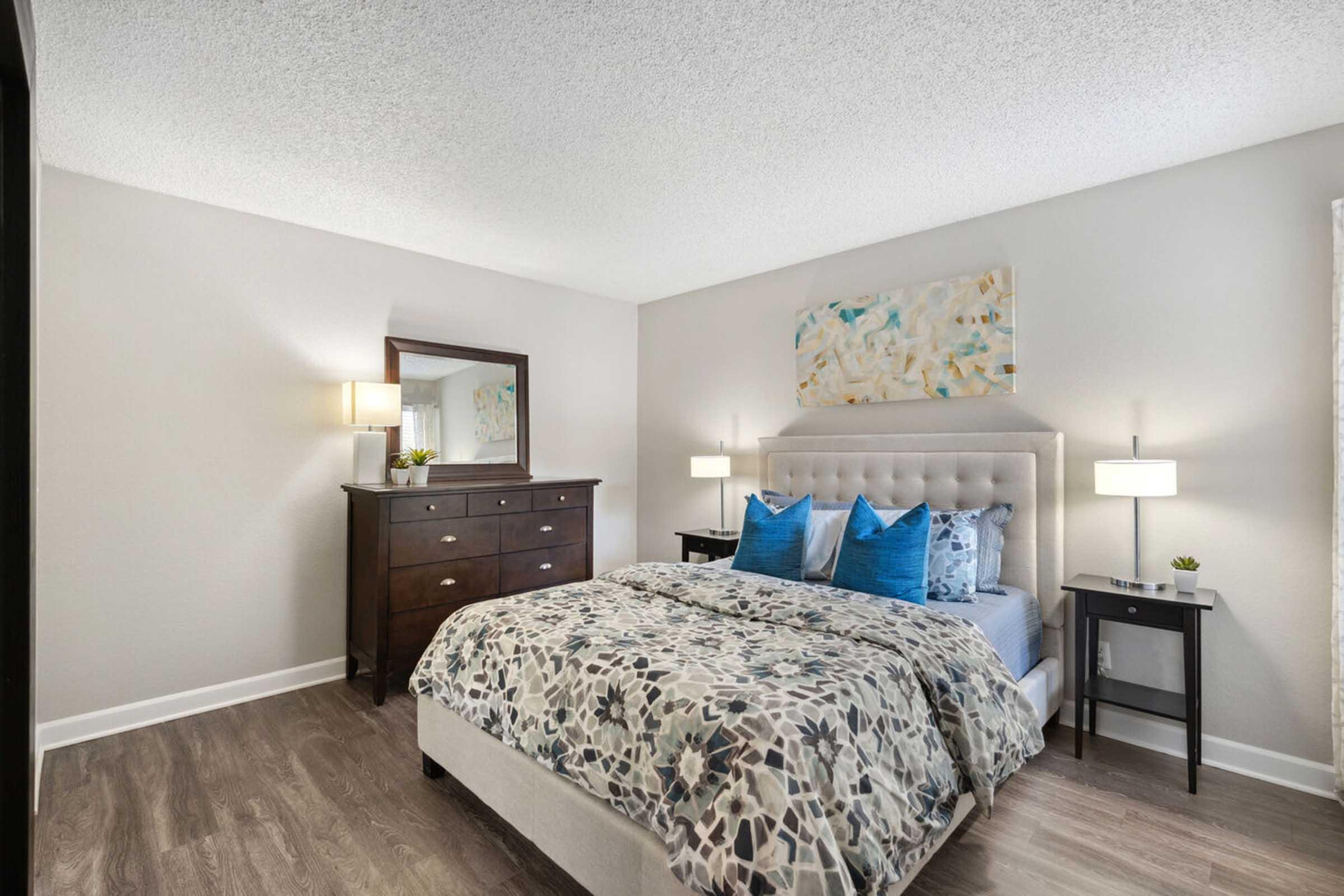 A modern bedroom featuring a queen-sized bed with a patterned duvet and blue accent pillows.