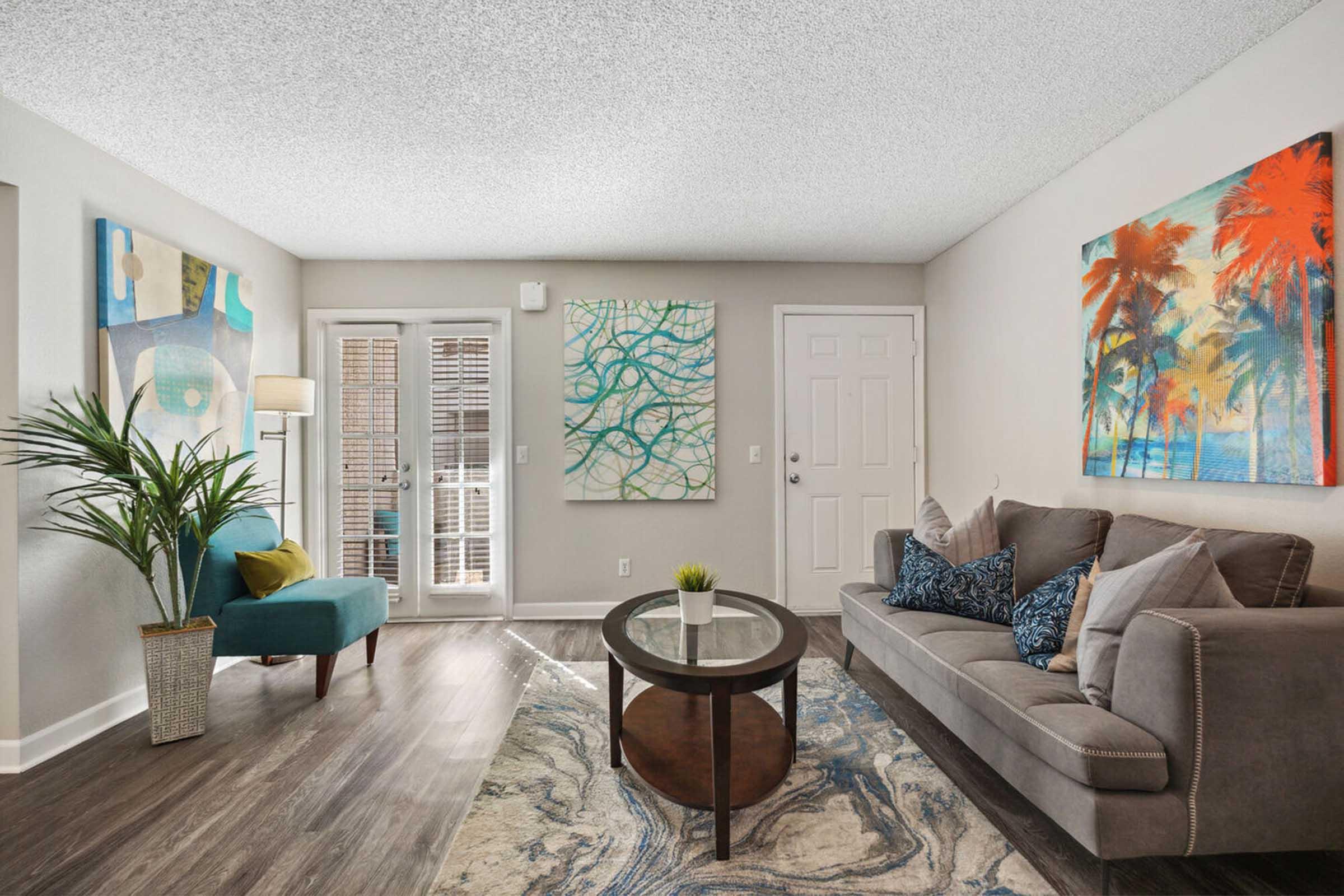 A modern living room featuring a grey sofa with decorative pillows, an accent chair in teal, and a round coffee table on a patterned area rug.