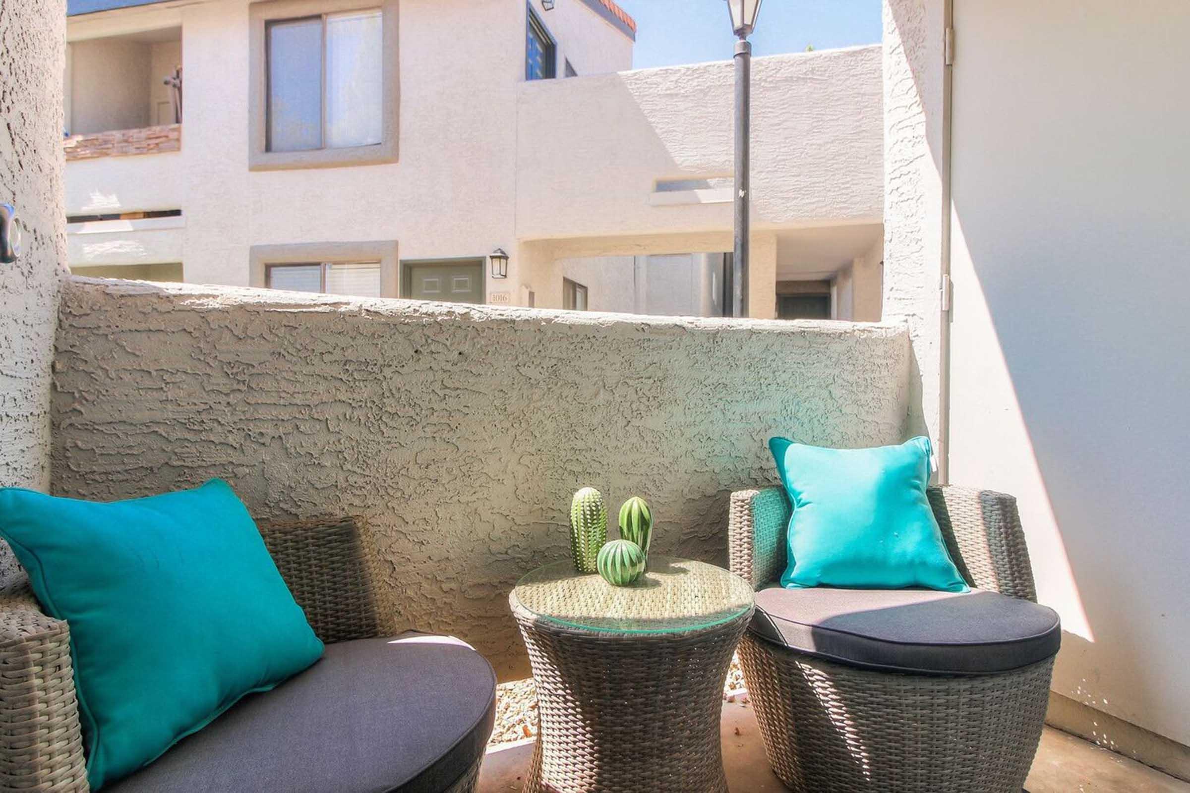 A cozy outdoor seating area featuring two woven chairs with bright turquoise cushions and a small round table.