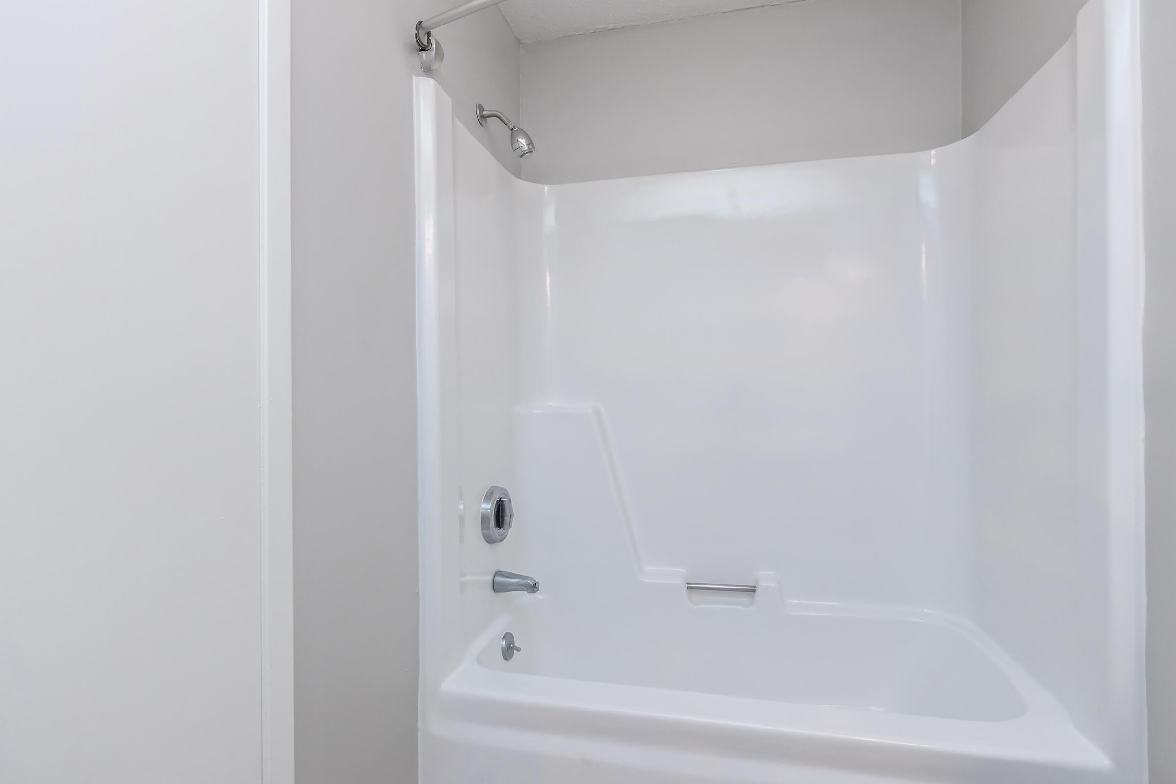 A clean, white shower stall with a built-in tub, featuring a handheld showerhead and a simple, modern design. The walls are smooth and light-colored, creating a bright and spacious feel. There are no visible fixtures or decorative elements in the image.